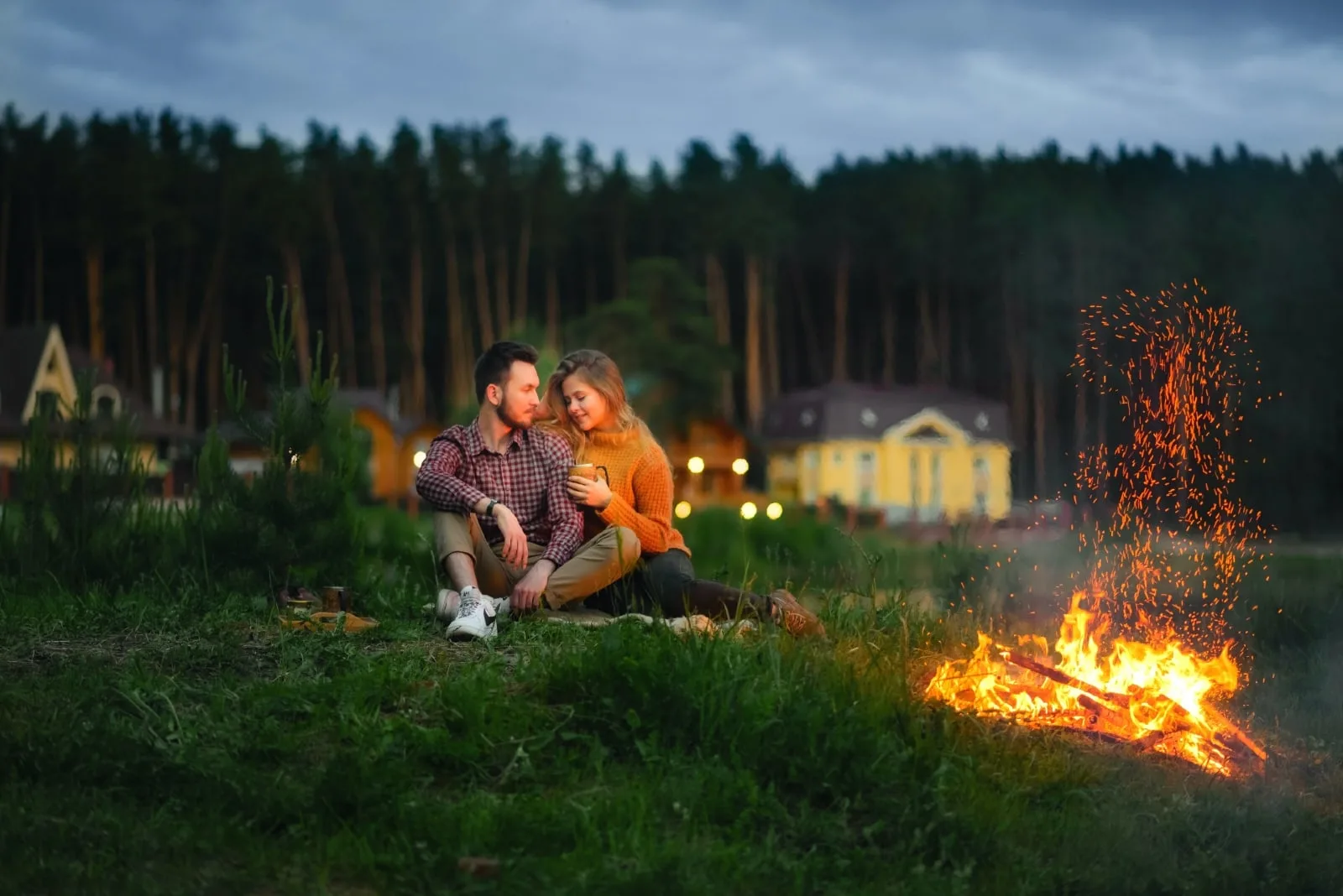 man and woman sitting on grass near fire pit