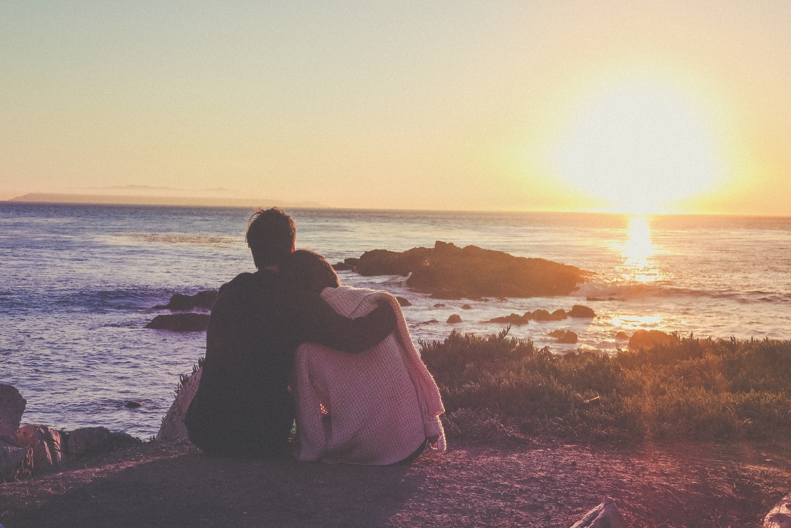 man and woman looking at sunset while sitting on ground
