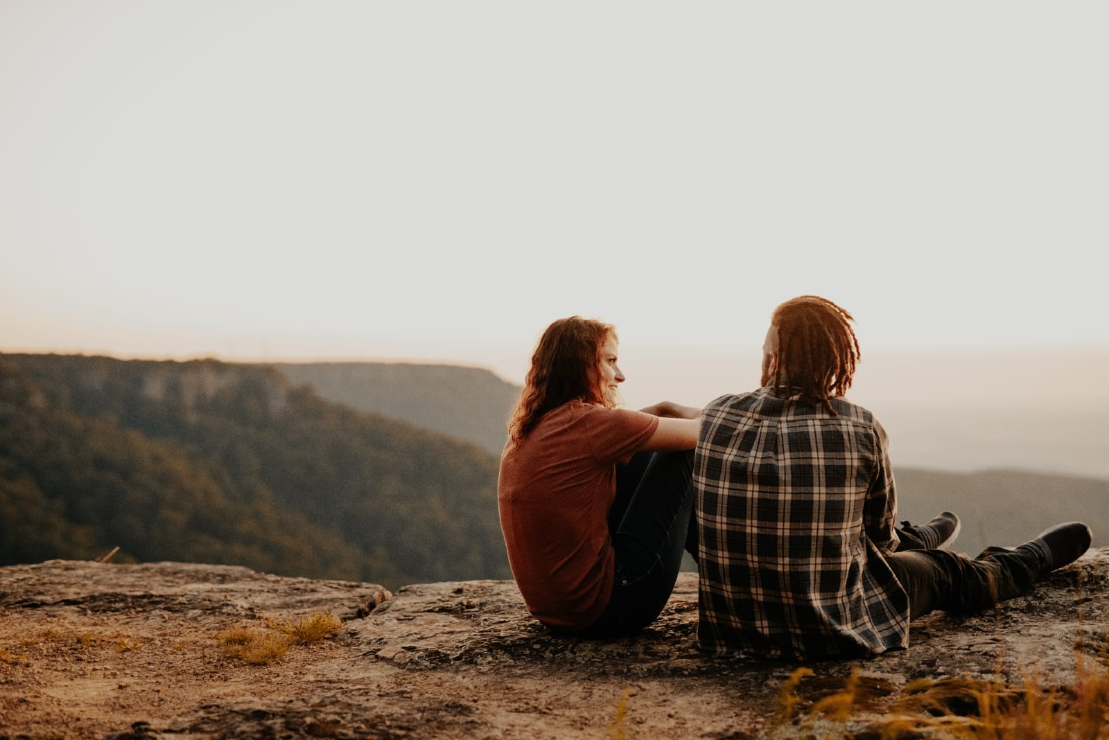 man and woman talking while sitting on rock