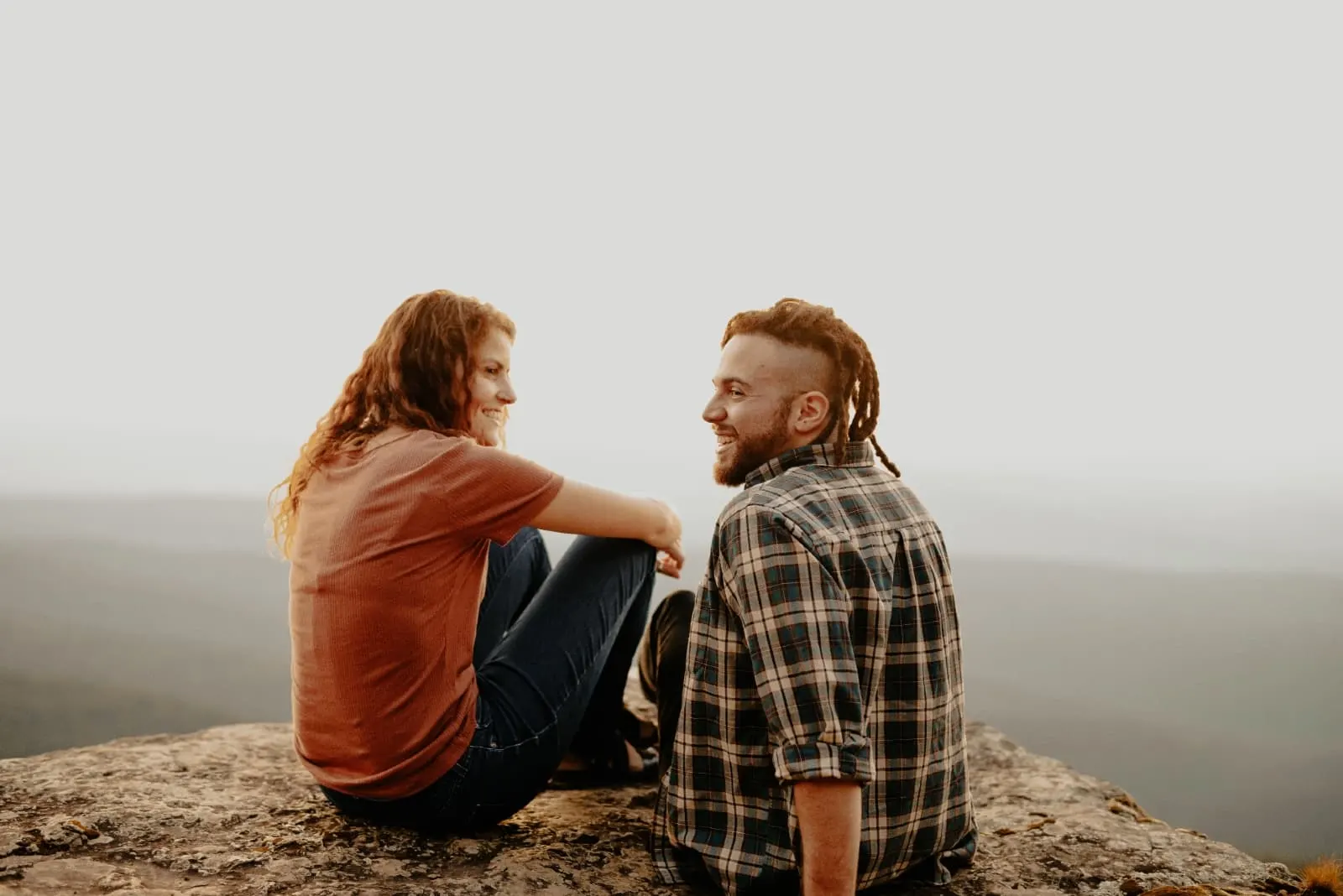 man and woman smiling while sitting on rock