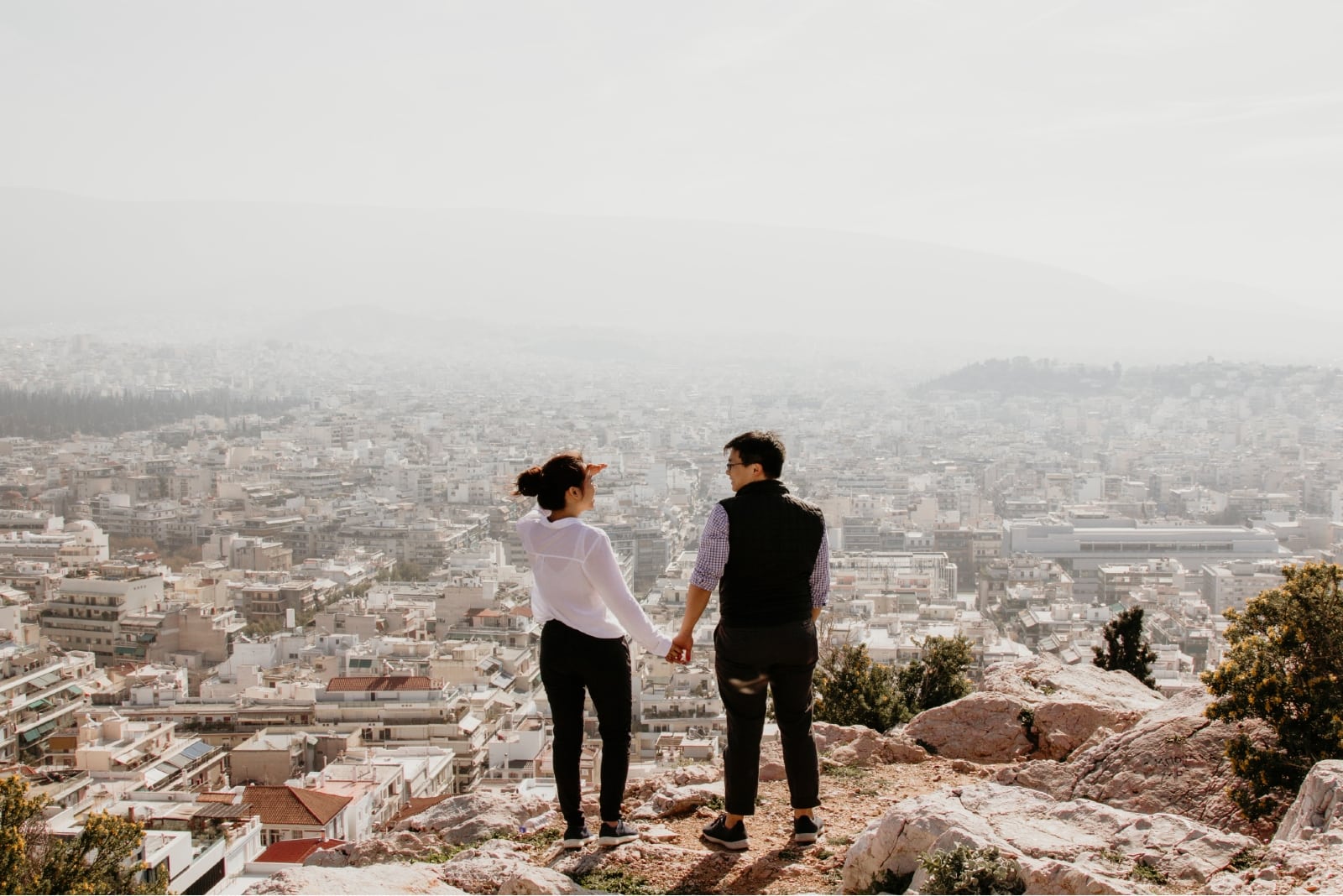 man and woman holding hands while standing on top of cliff