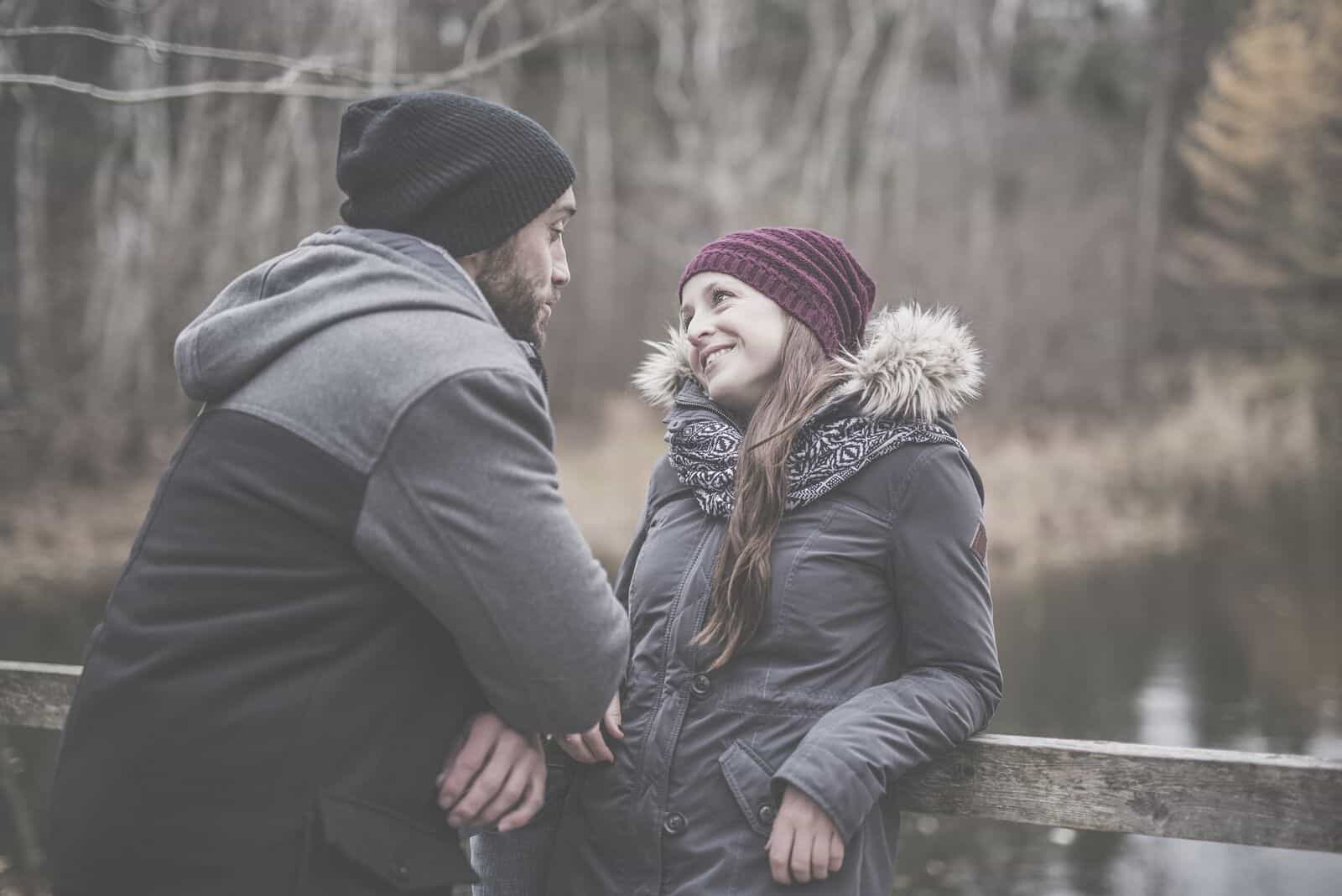 pareja hablando en invierno al aire libre de pie y apoyada en una barandilla de madera