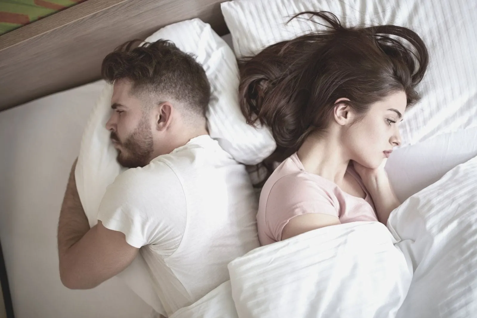 couple with relationship problems lying down in bed facing each others side of the bed