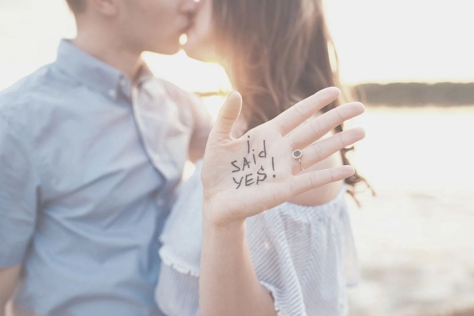 cropped image of a couple kissing in the golden hour with woman showing hand with words i said yes