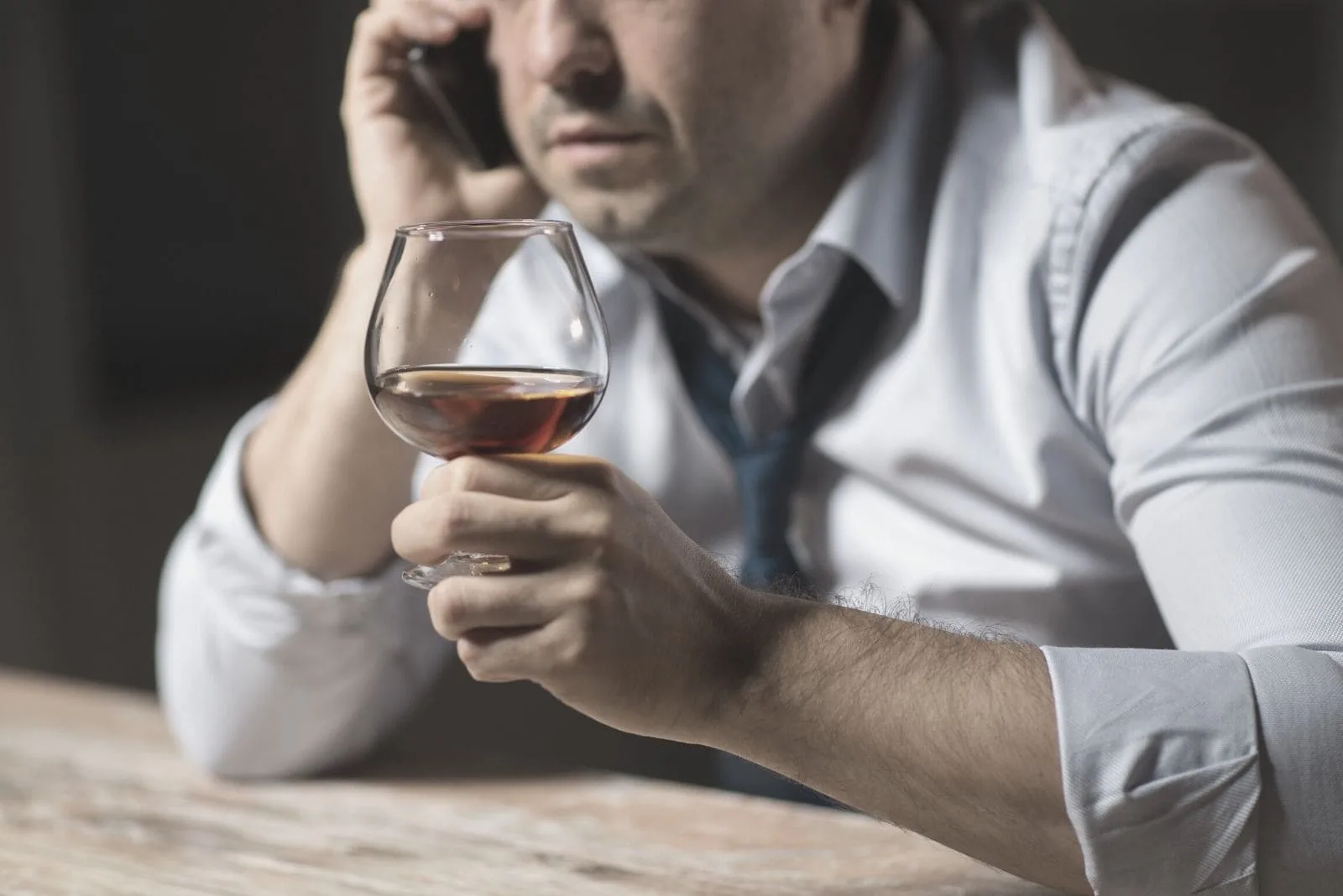 cropped photo of a man drinking alcohol while calling by the phone