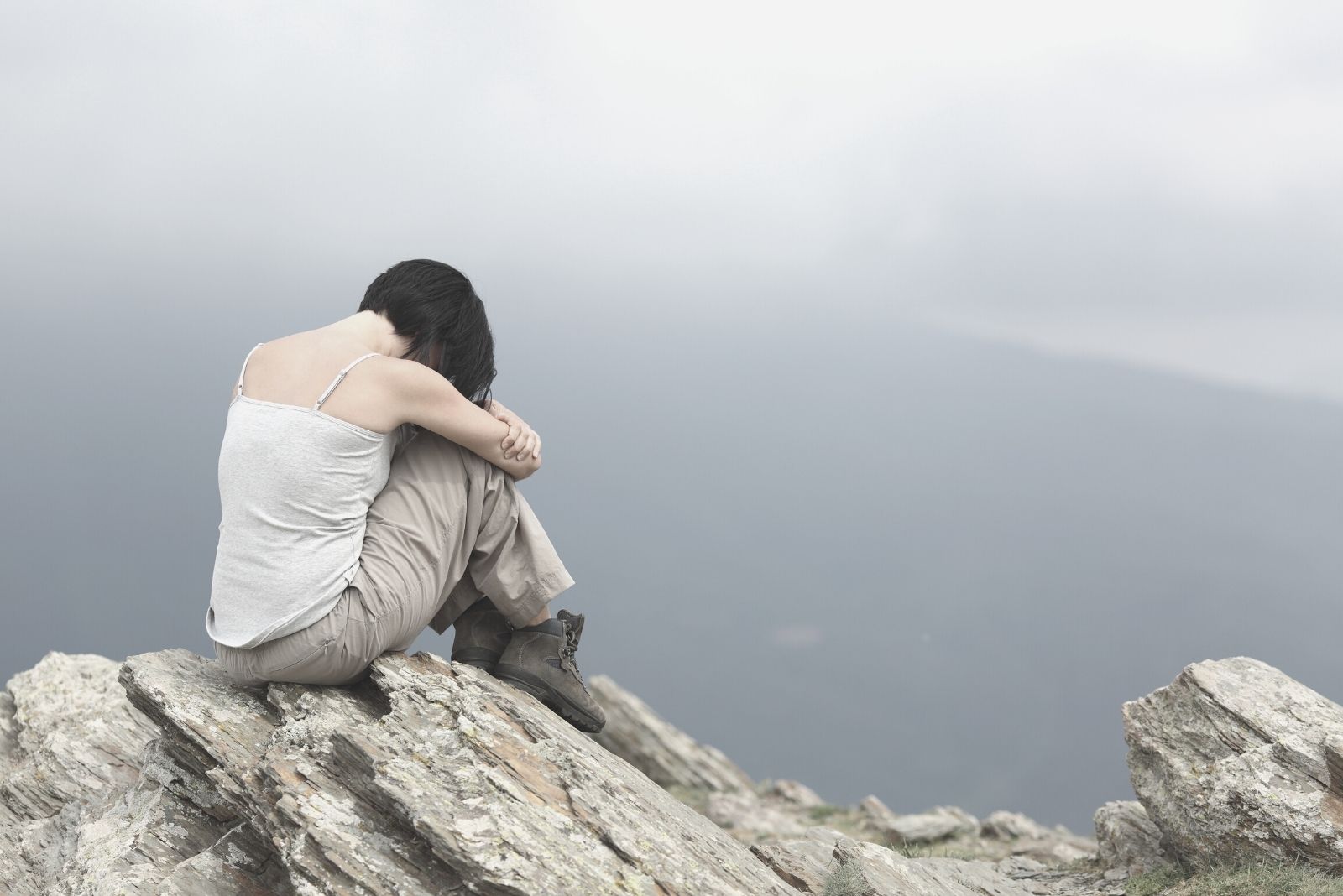 donna depressa e triste seduta in cima alla montagna con la faccia rivolta verso il basso abbracciando le ginocchia