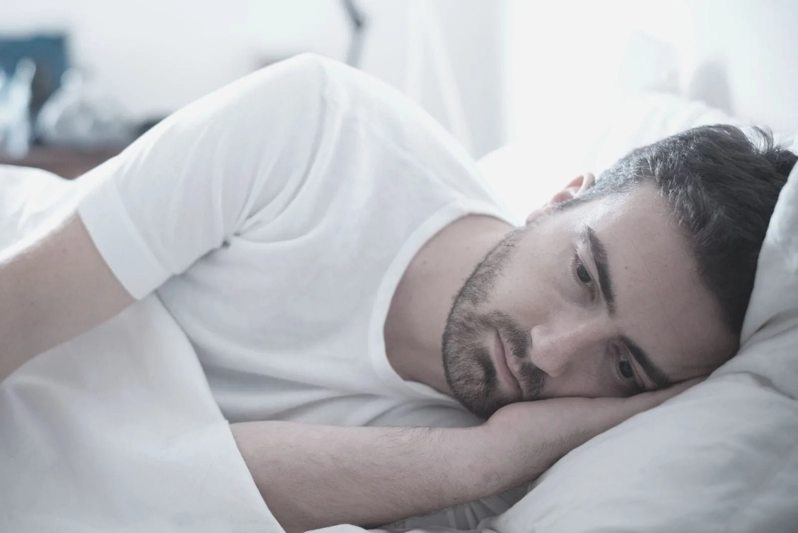 depressed man lying down on bed facing his left side of the bed