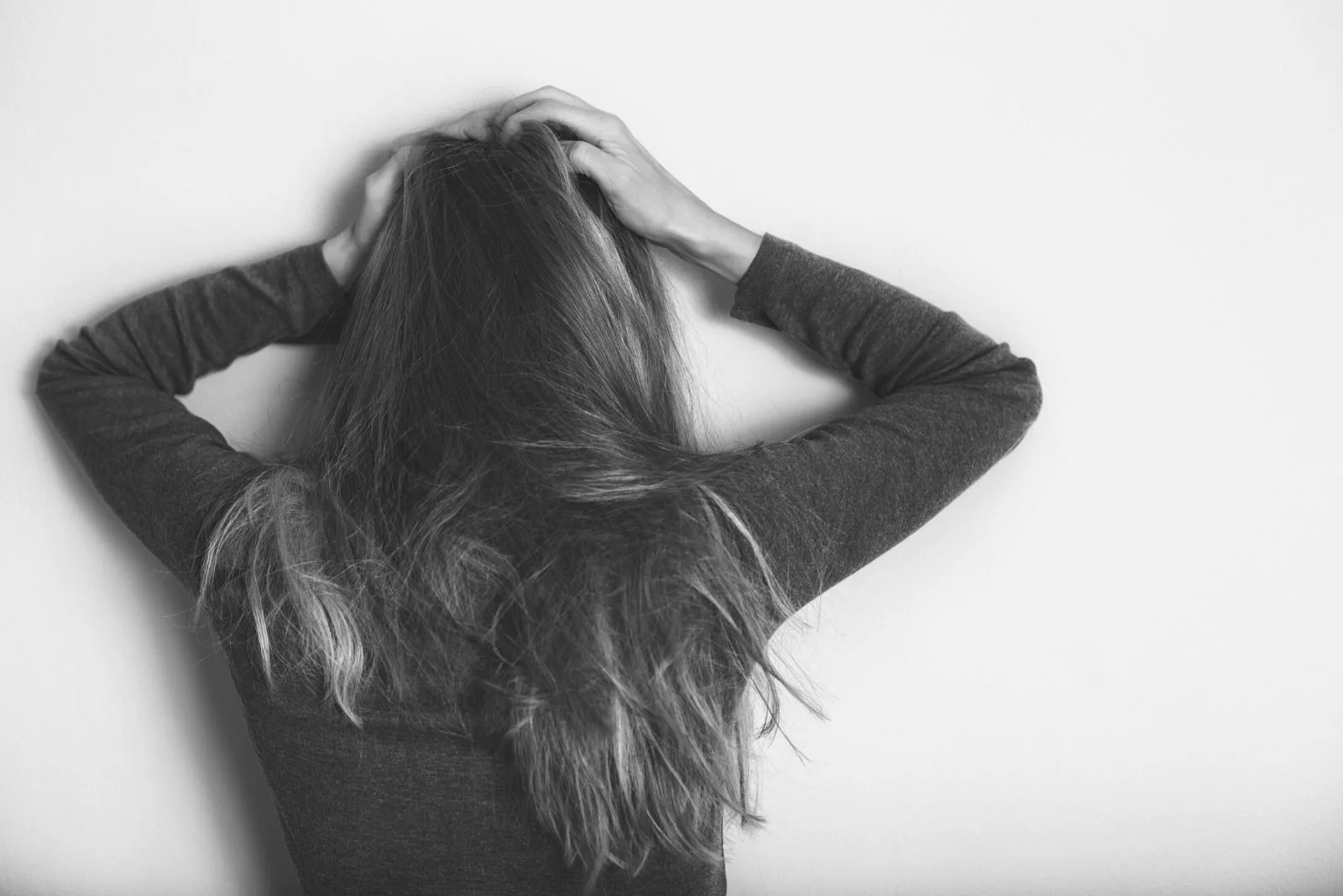 depressed woman standing against the wall alone holding her head in toned image