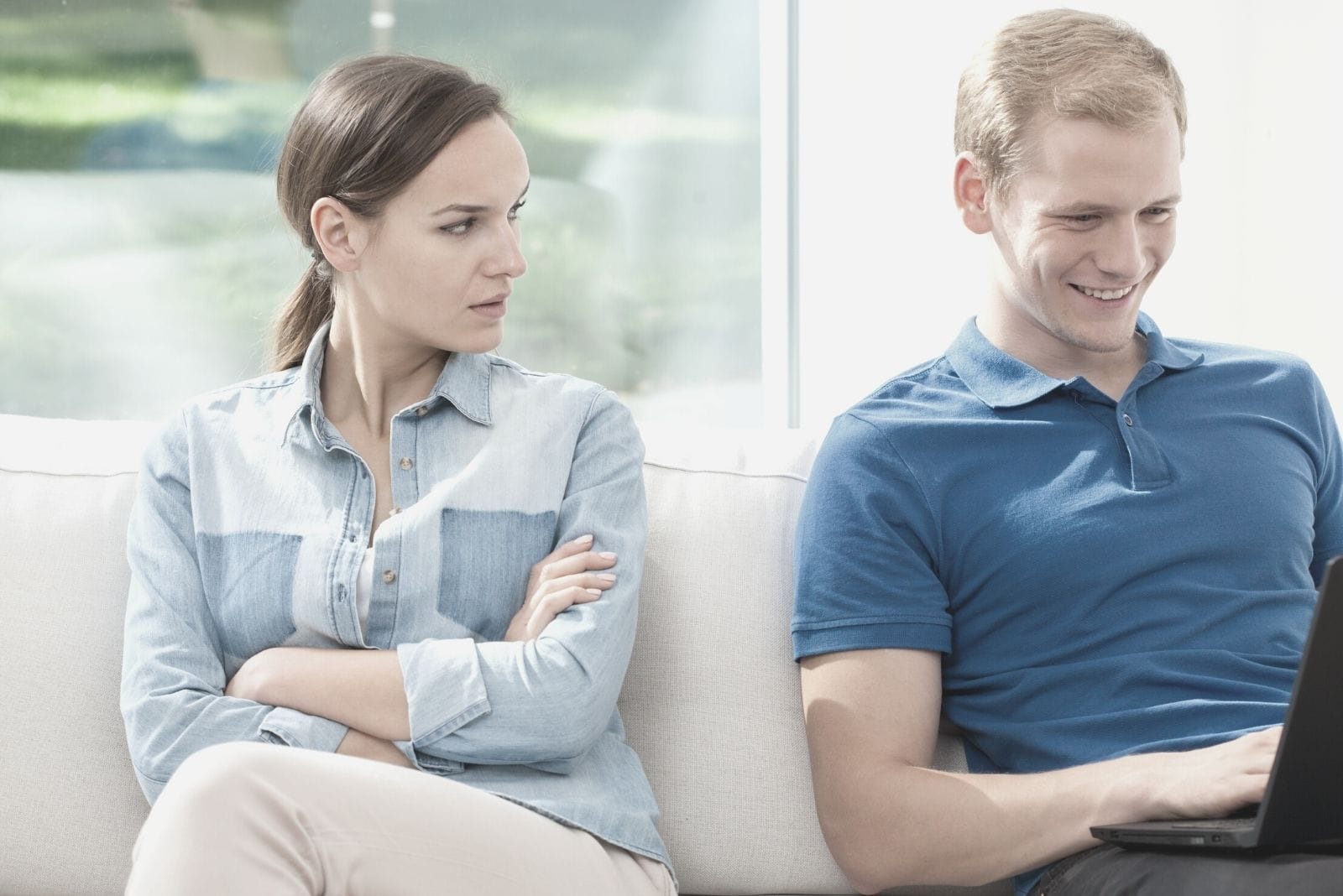 disguted woman sitting beside a computer addict man inside the living room