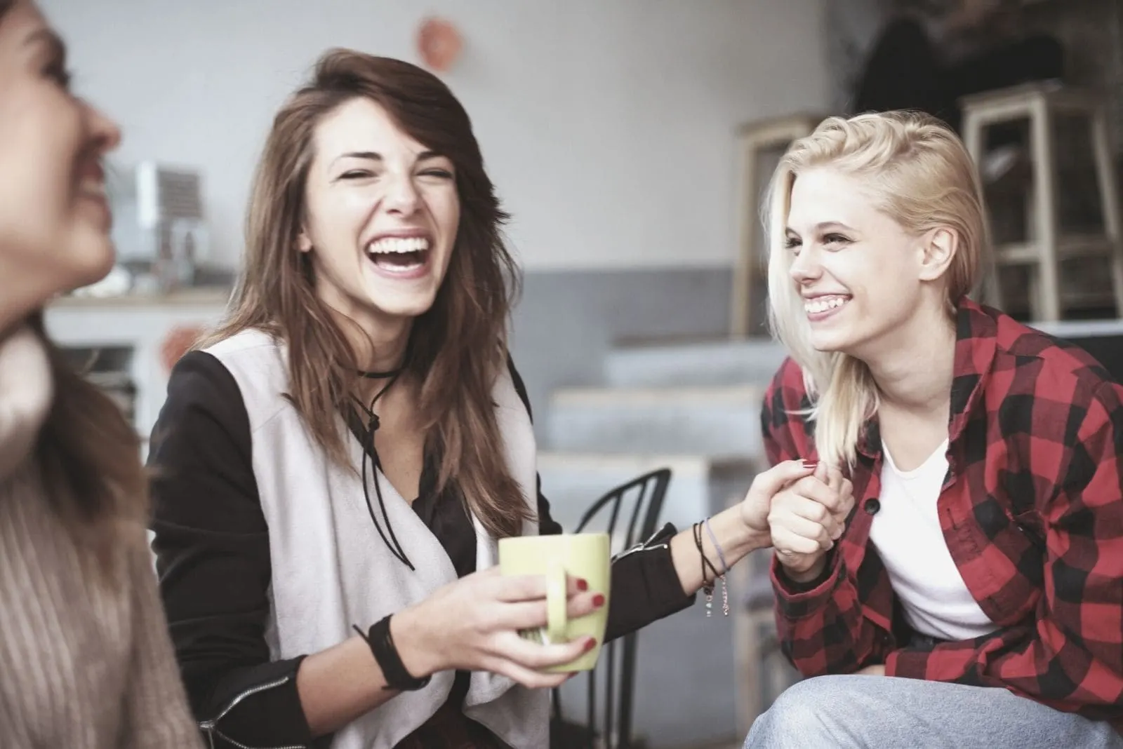 female friends laughing and chatting inside the living room while drinking coffee