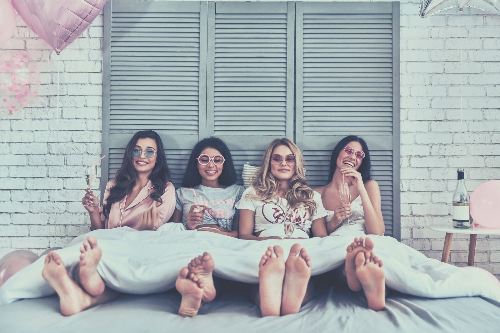 quattro giovani donne attraenti in camicia da notte sedute sul letto a bere un cocktail