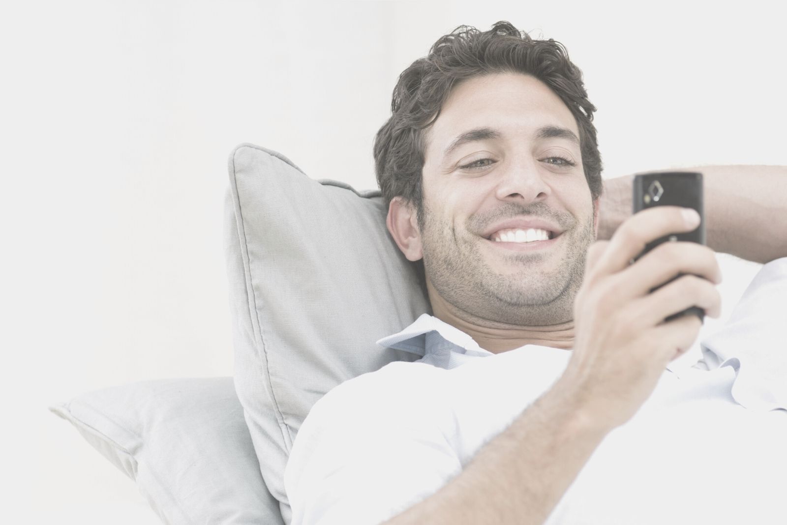 uomo sorridente sdraiato mentre legge un messaggio dal suo cellulare