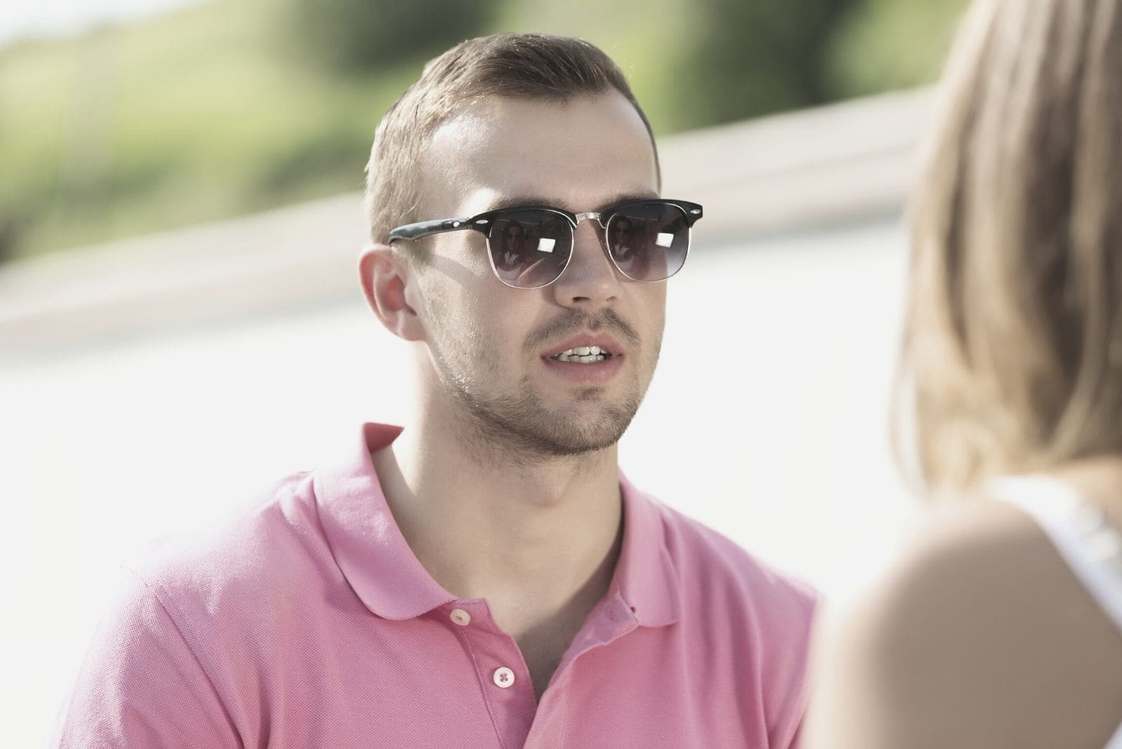 handsome young man wearing pink top and sunglasses talking to a woman outdoors