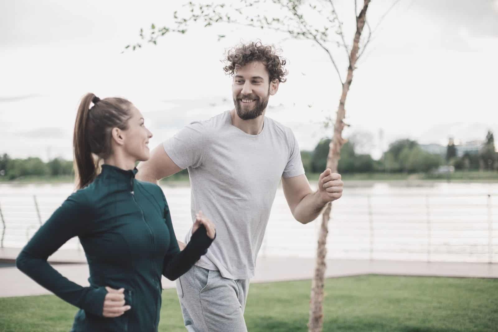 Feliz pareja de atletas corriendo y charlando cerca de la masa de agua