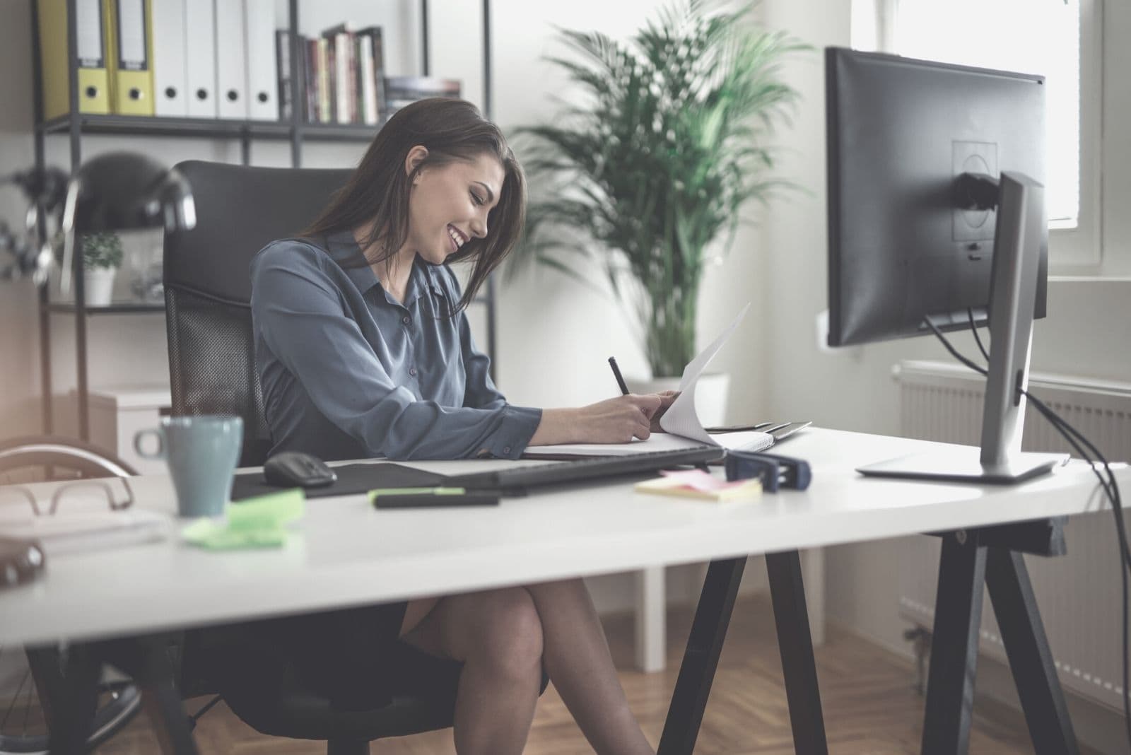 mulher de negócios feliz a trabalhar no escritório, sentada à mesa e a escrever