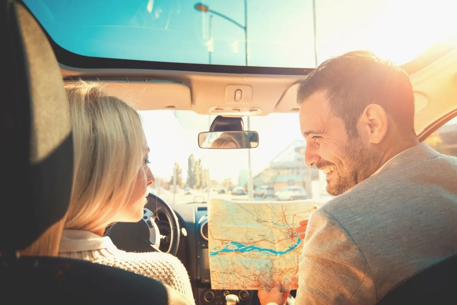 happy couple travelling together inside a car holding a map