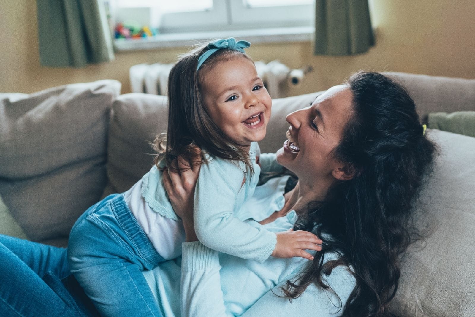 mãe feliz a brincar com a filha no sofá da sala de estar