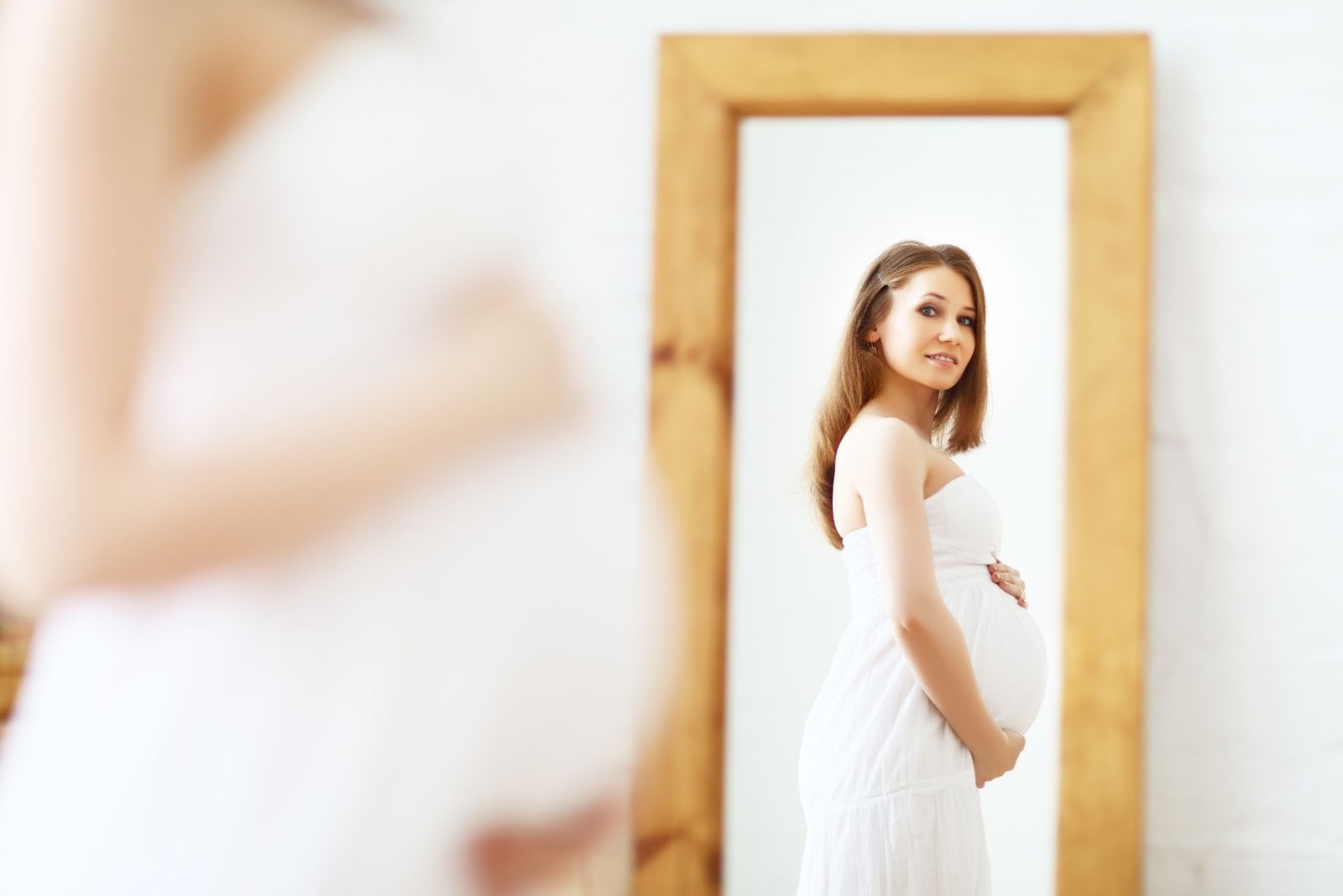 happy pregnant woman looking at her baby bump on the mirror