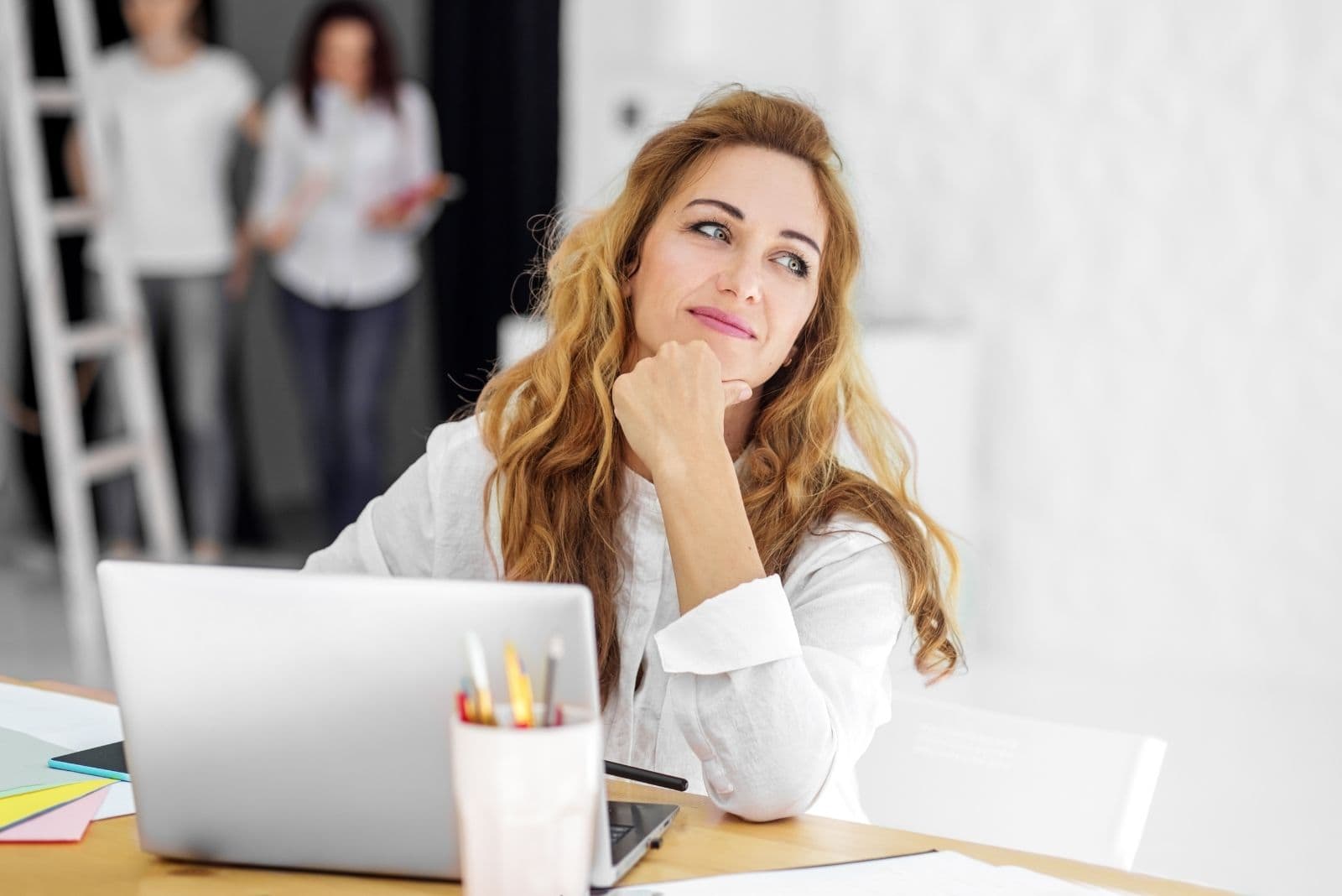 Donna felice che lavora all'interno dell'ufficio con due colleghi sullo sfondo nella fotografia sfocata