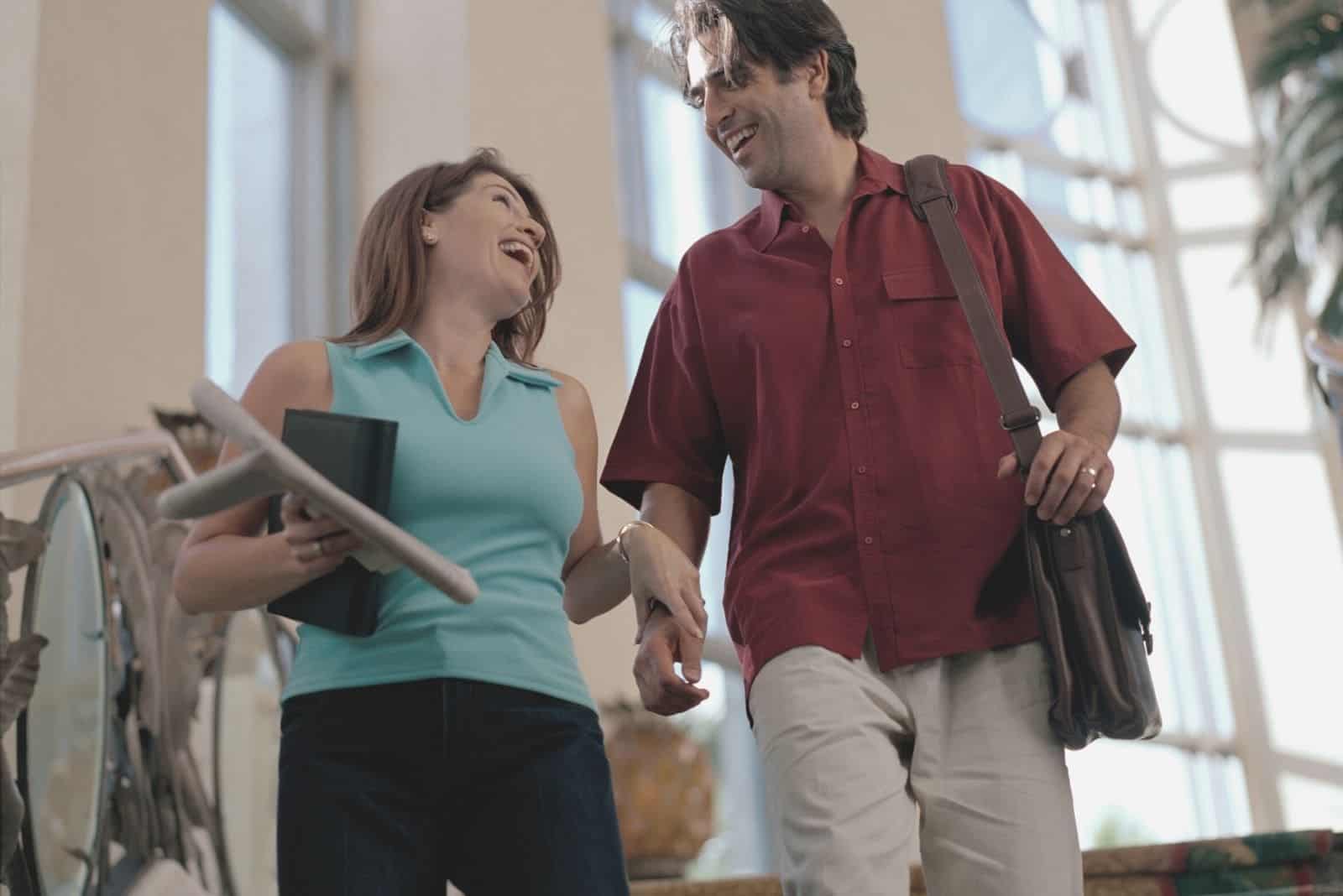 heterosexual couple laughing while walking down the stairs and bringing their stuffs