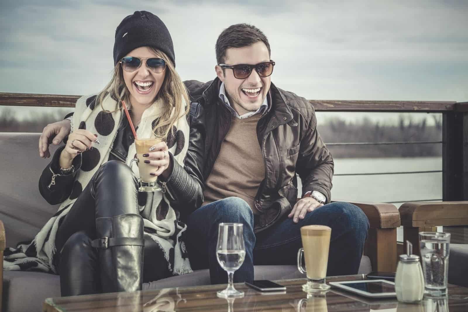 man and woman laughing while drinking with river in the background