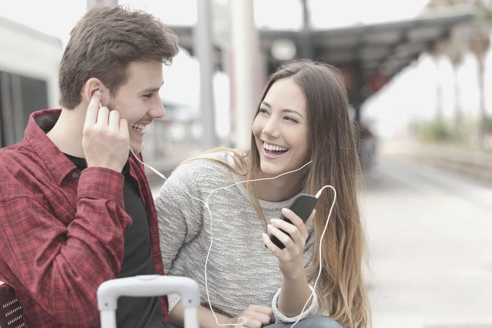 hombre y mujer escuchando la música en el teléfono sentados al aire libre