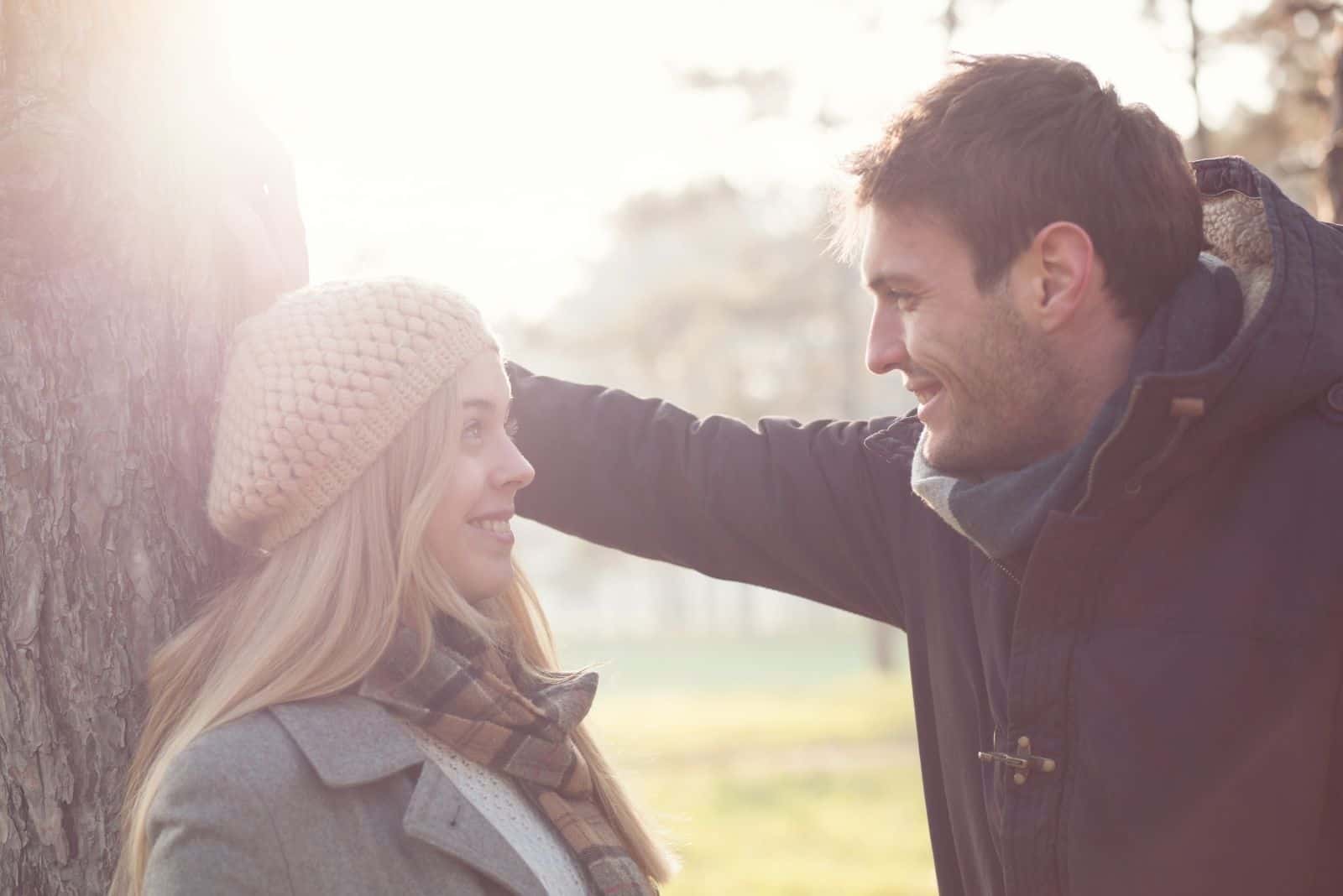 man and woman outdoors leaning on the tree smiling