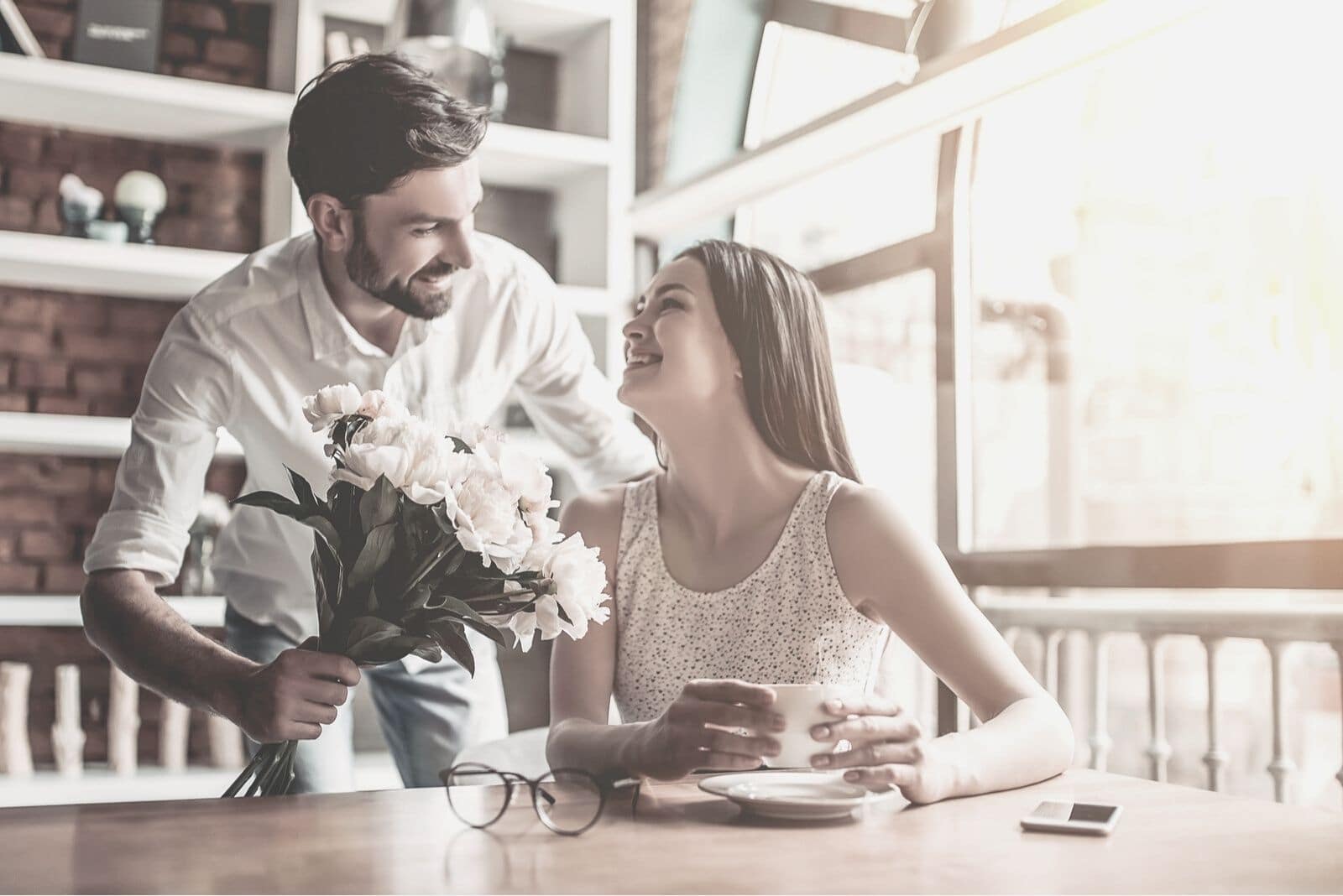 man giving a bouquet of flowers to the woman in the coffee shop looking happy and surprised