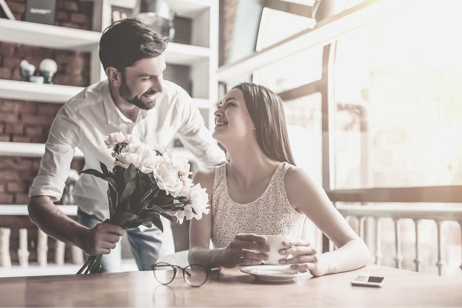 hombre dando un ramo de flores a la mujer en la cafetería mirando feliz y sorprendido