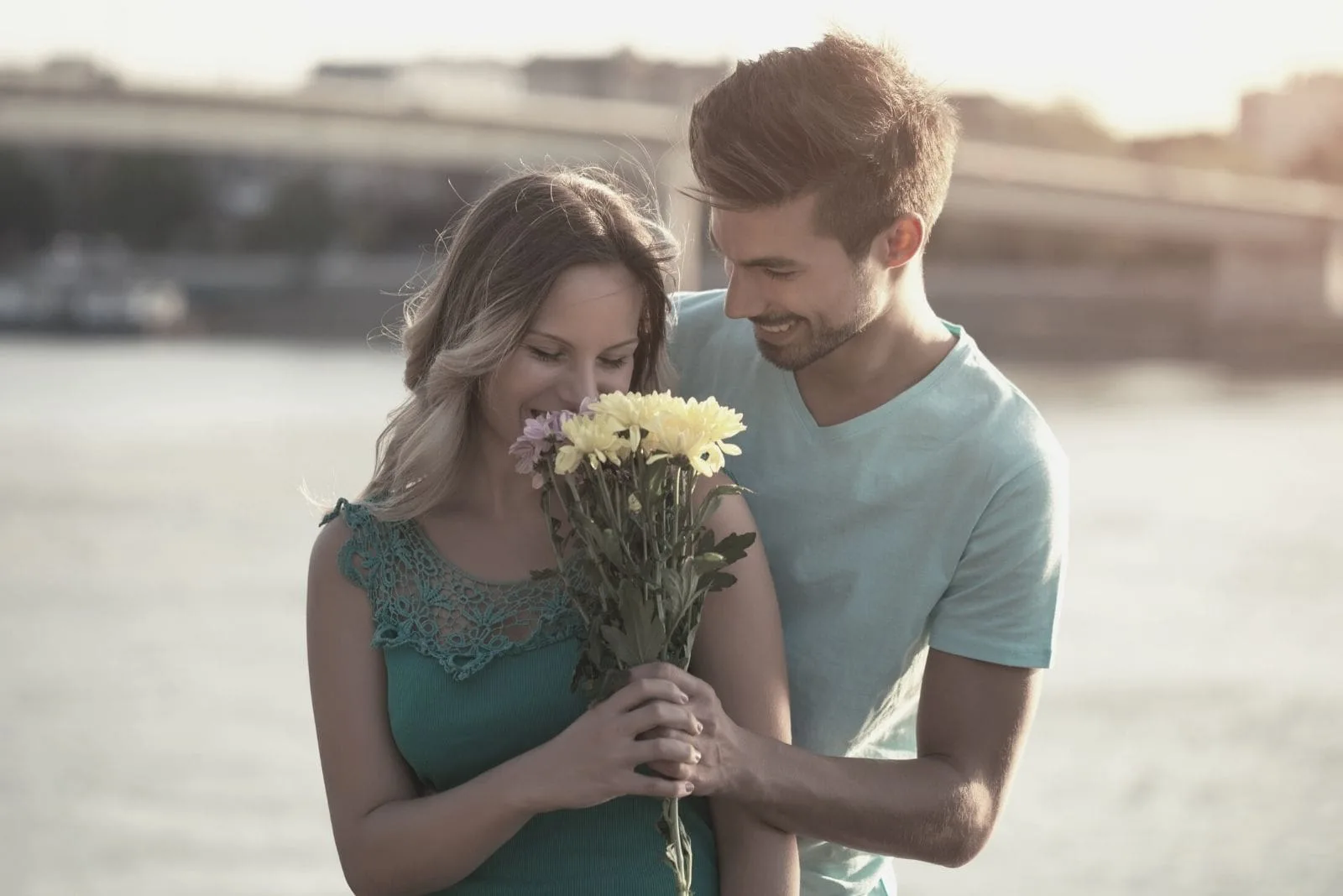 man giving flowers to his girlfriend while standing near the body of water