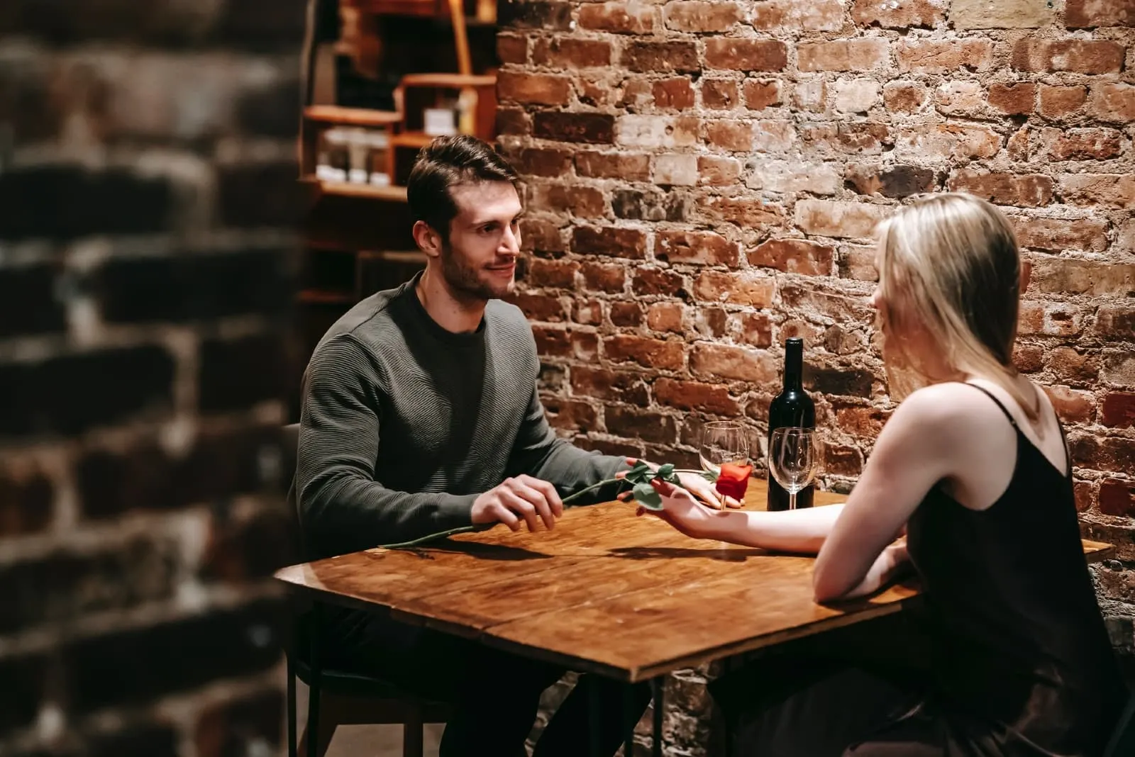 man giving rose to woman while sitting at table