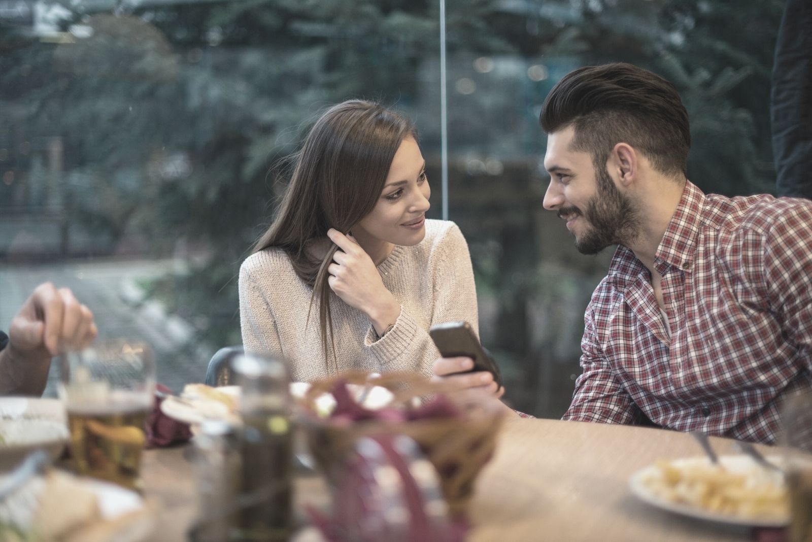 man holding a phone while sitting next to a woman in the restaurant