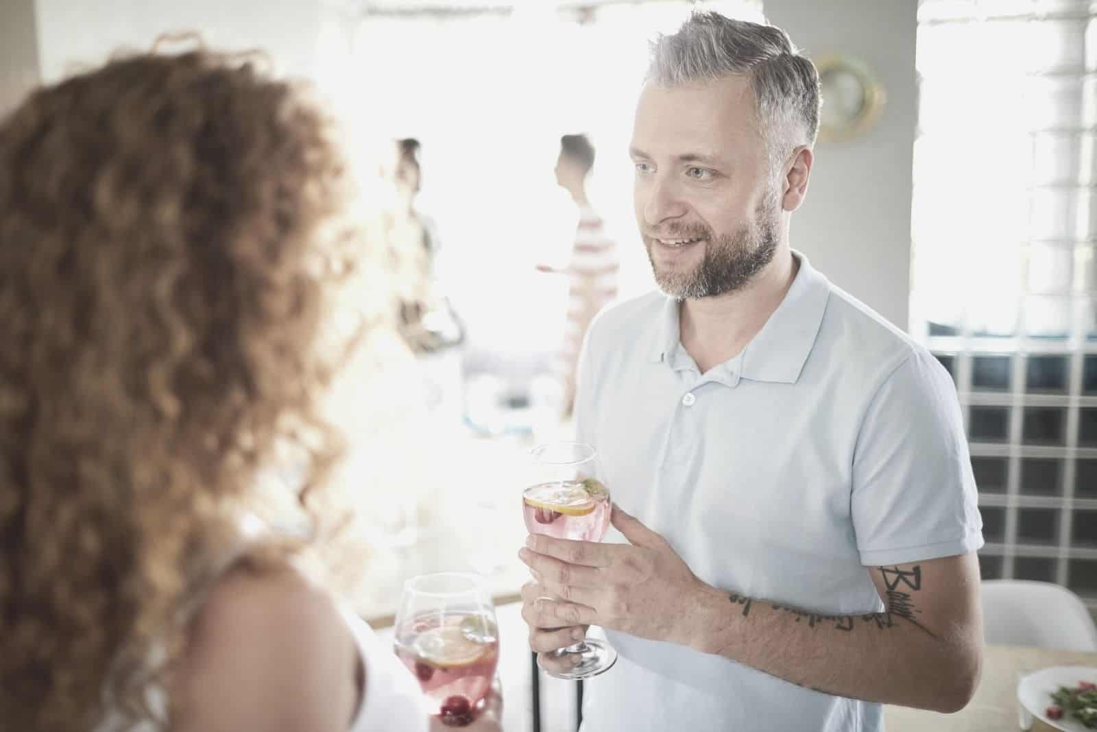 uomo che tiene in mano del vino mentre parla con una donna con i capelli ricci in una riunione