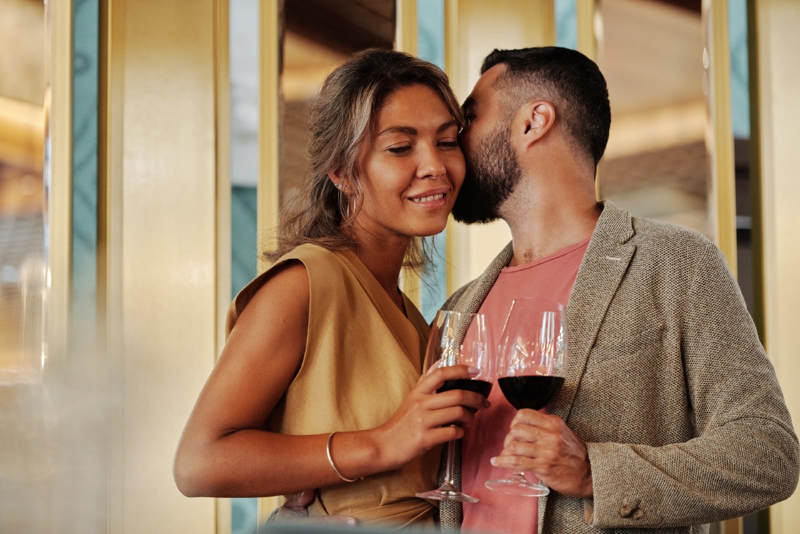 man kissing woman while holding glass of wine