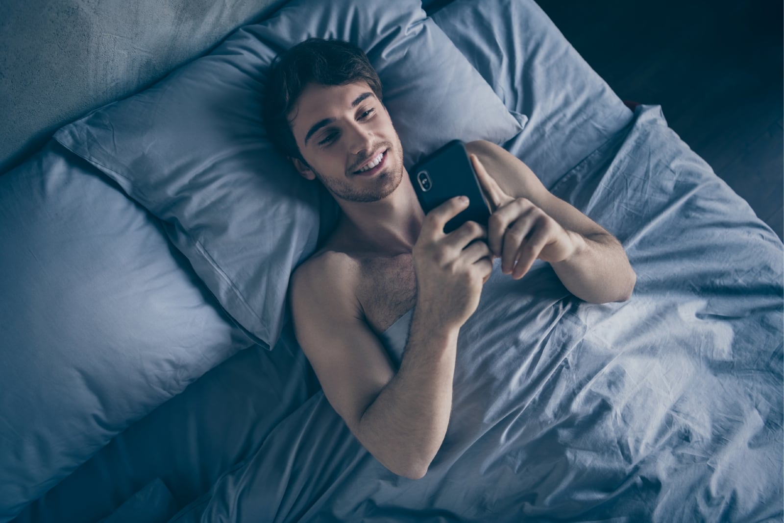 homem feliz deitado na cama enquanto utiliza um smartphone