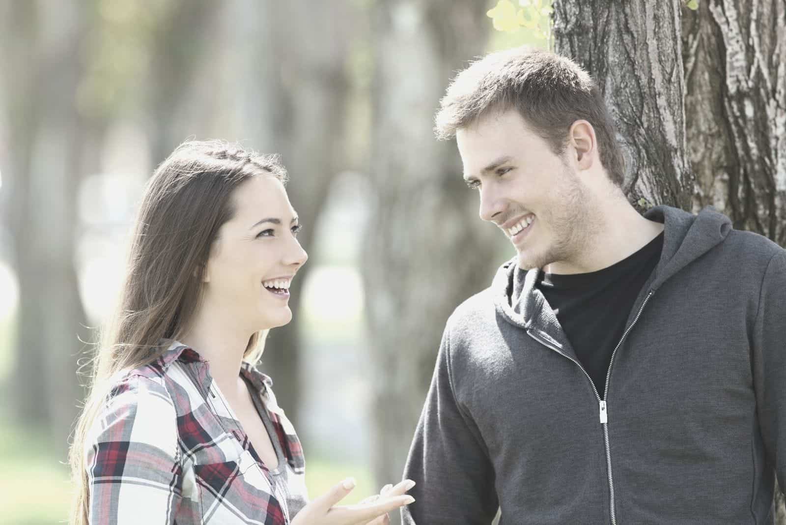 Mann lehnt am Baum und spricht und lacht mit einer schönen Frau