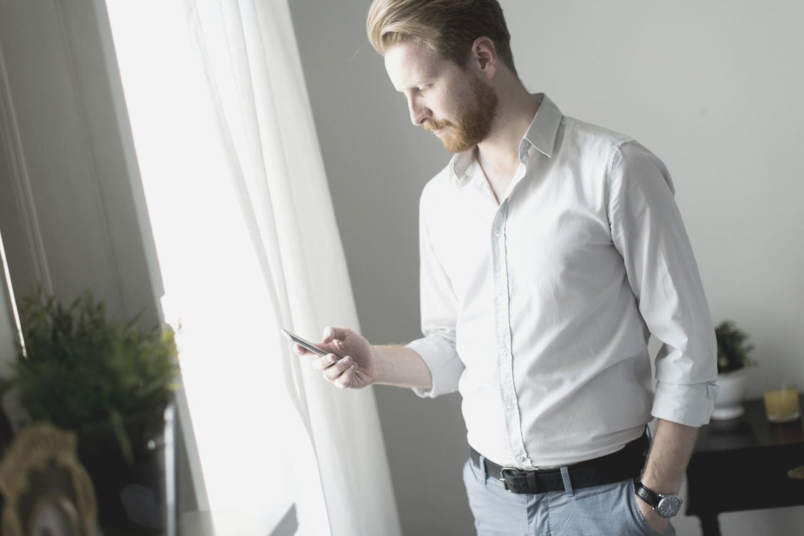 man looking at his phone with one hand on his pocket while standing inside a room