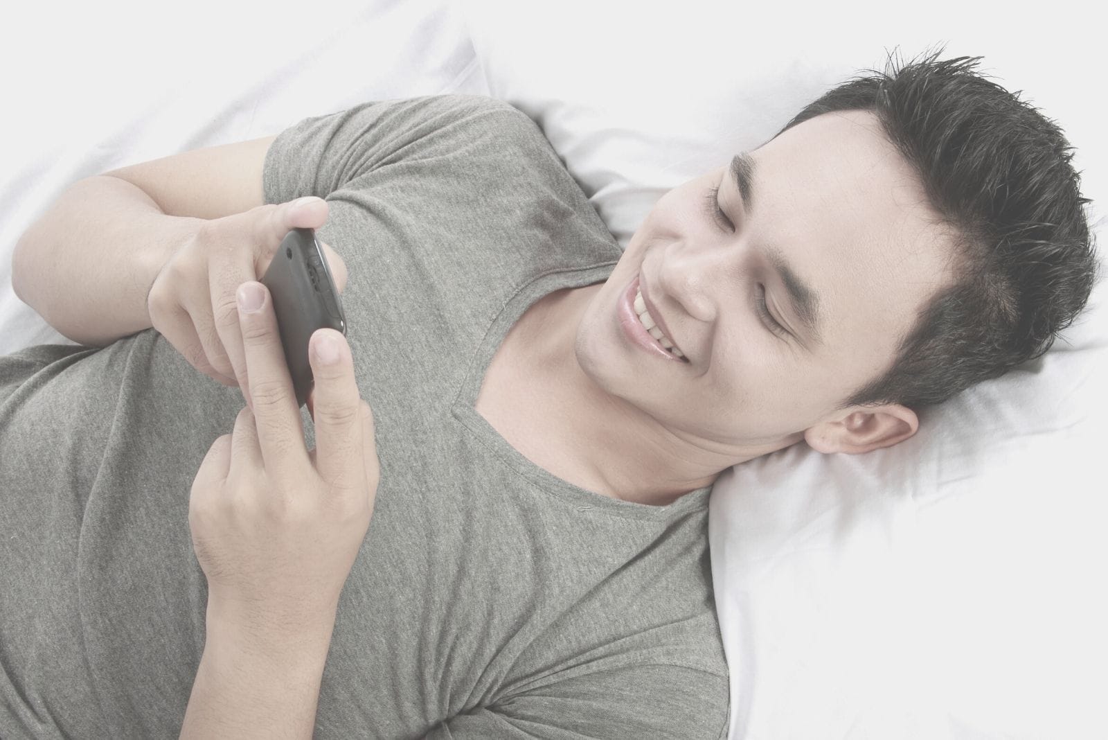 man lying down in bed texting and smiling