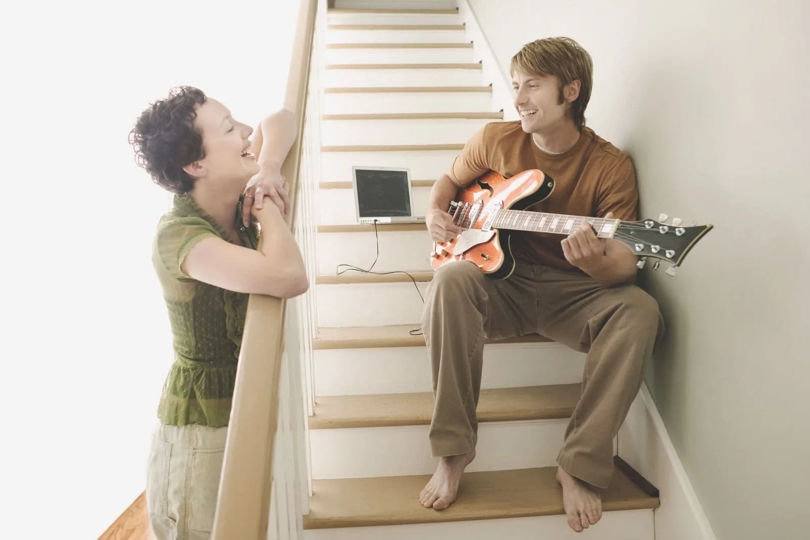 man playing guitar and sitting in the stairs while talking to the woman laughing