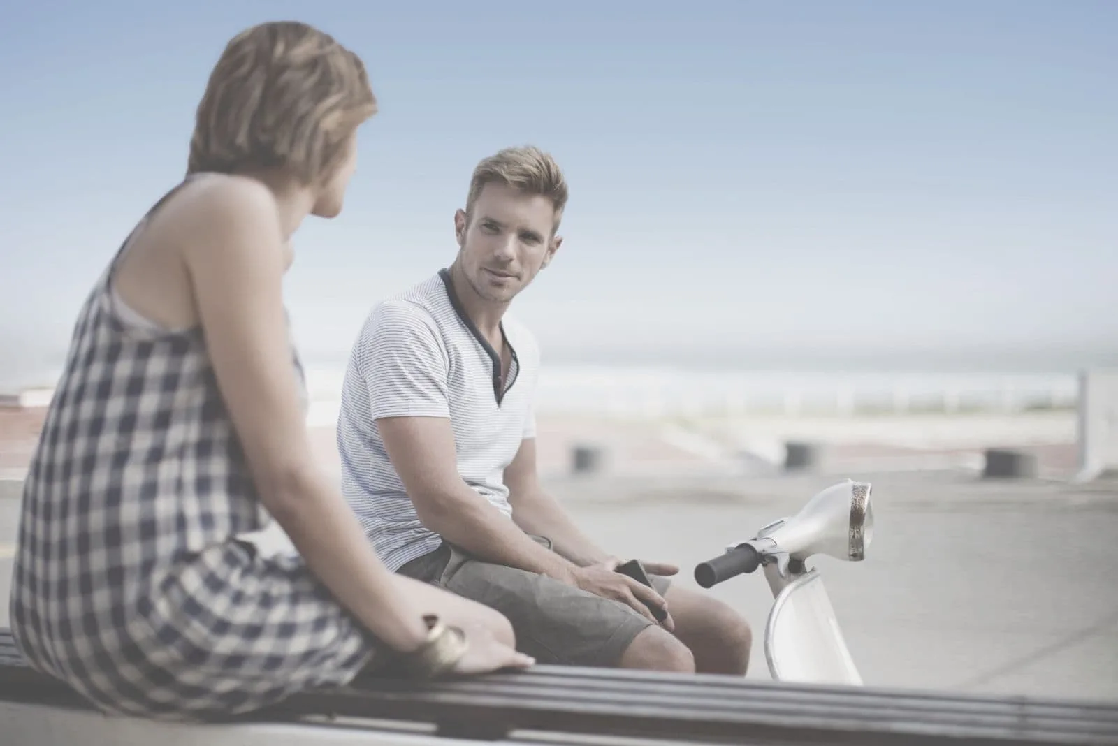 man sitting on a scooter talking to a woman sitting on the bench outdoors