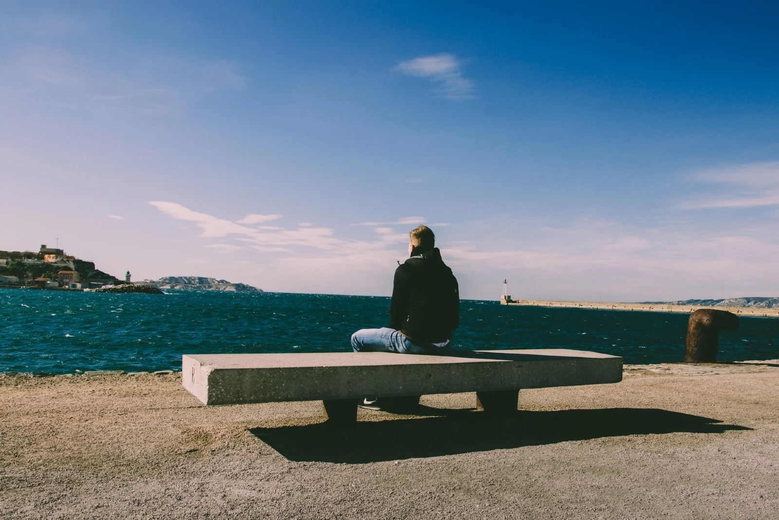 man sitting on bench while looking at sea