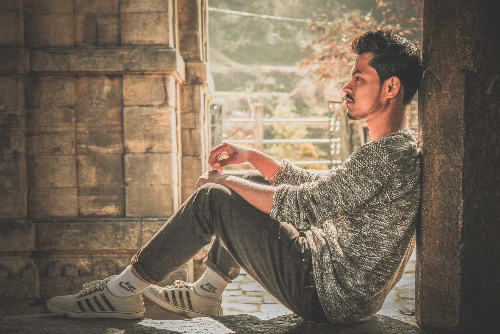 man in gray sweater sitting on concrete surface