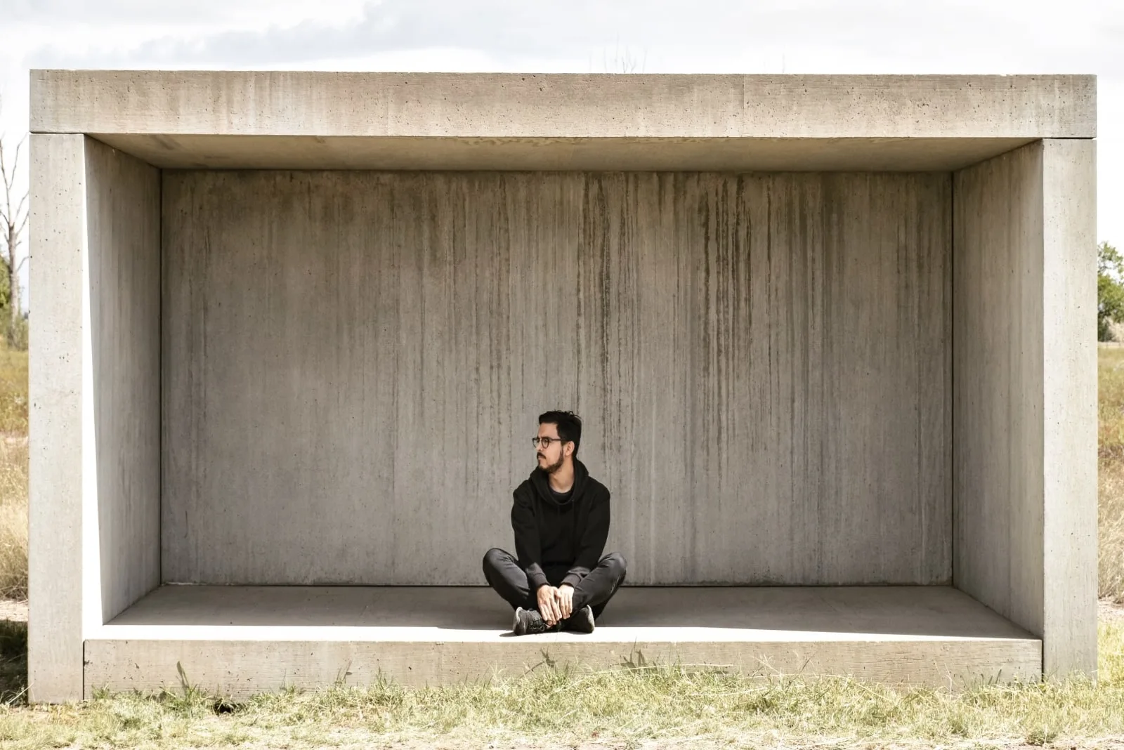 man in black hoodie sitting on concrete surface