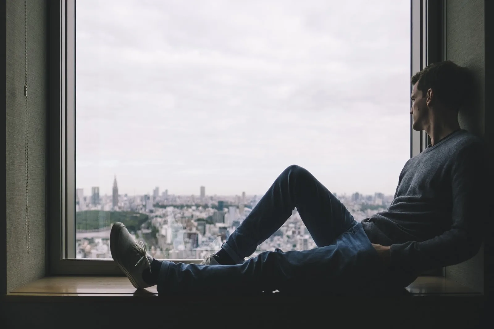 man sitting on window pane looking at city