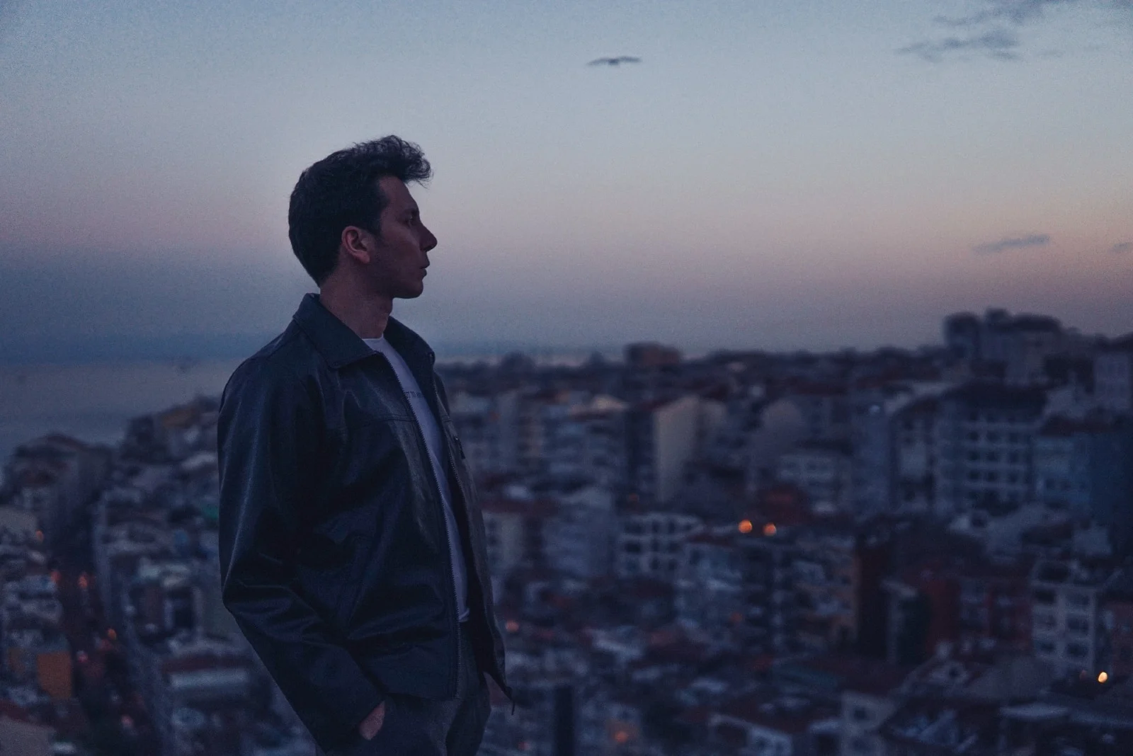 man in black jacket standing on rooftop during sunset