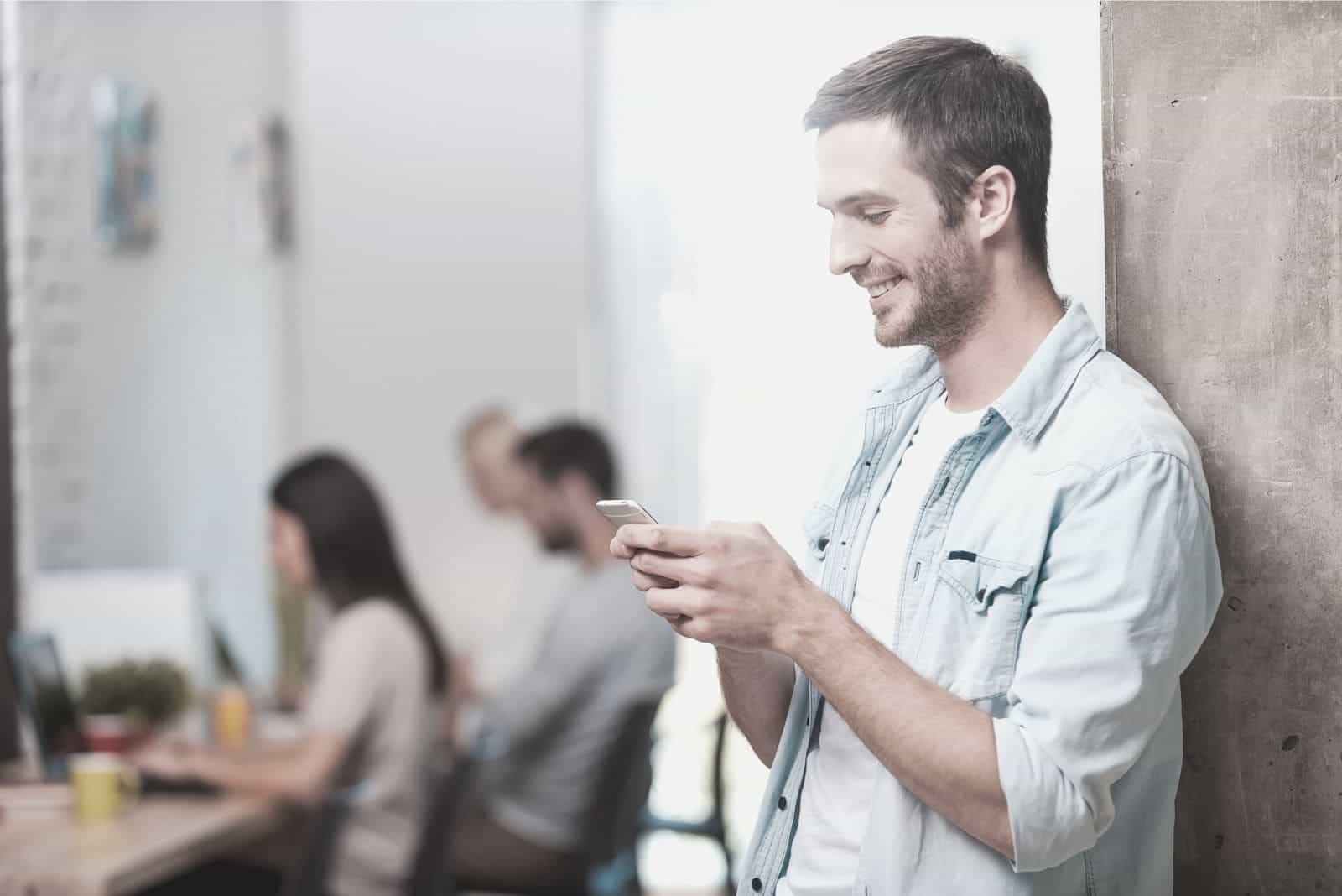 uomo che messaggia all'interno dell'ufficio con i colleghi impegnati a lavorare al tavolo