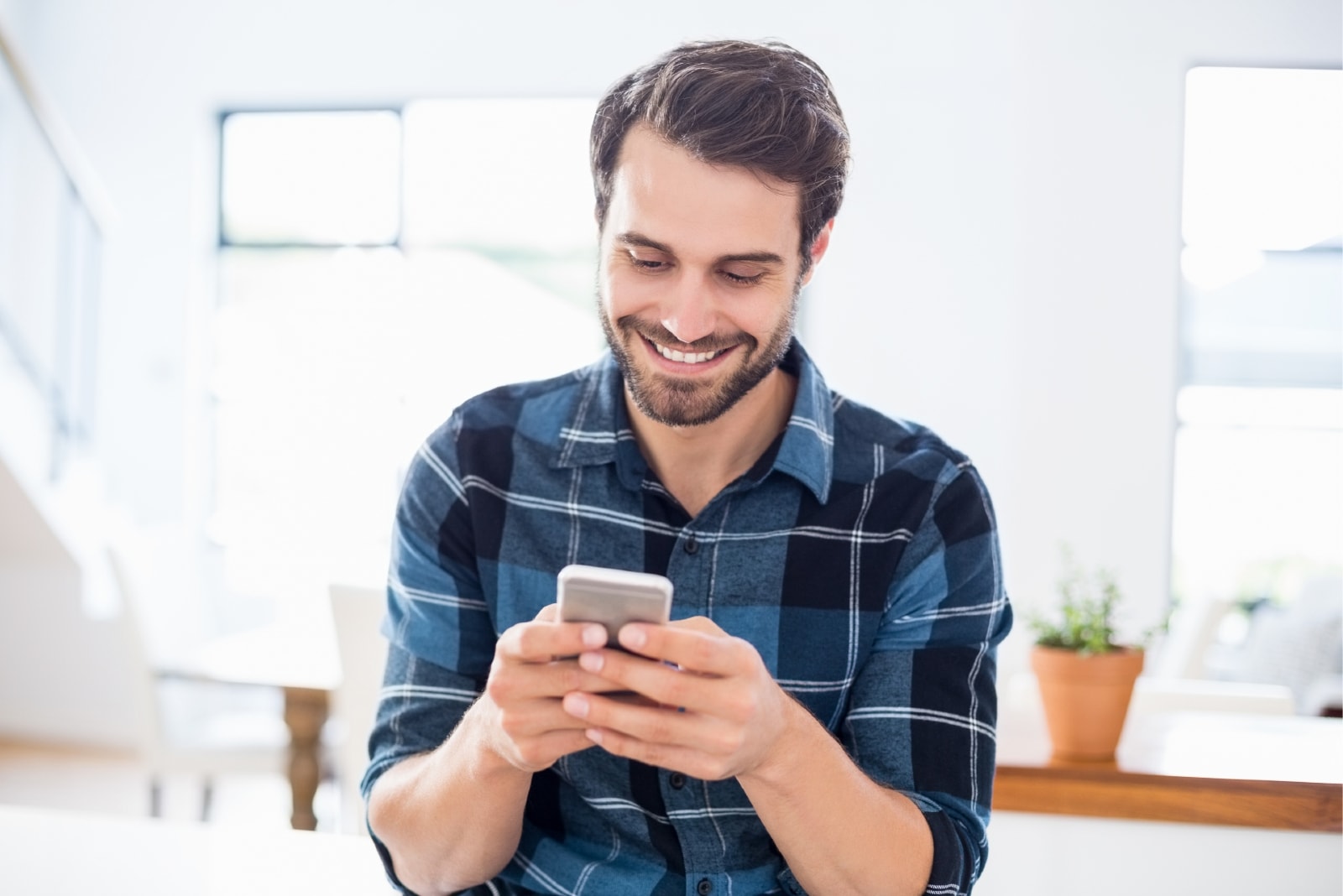 hombre feliz con camisa azul a cuadros usando el teléfono en interiores