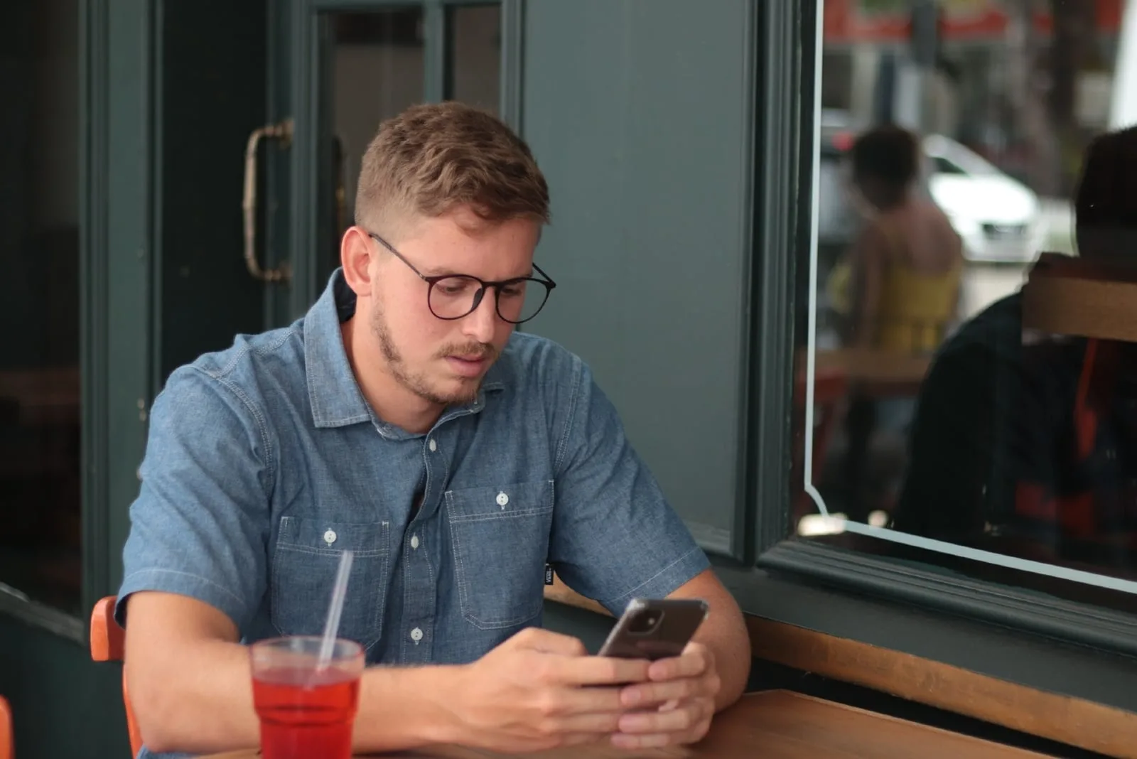 man with eyeglasses using smartphone while sitting at table