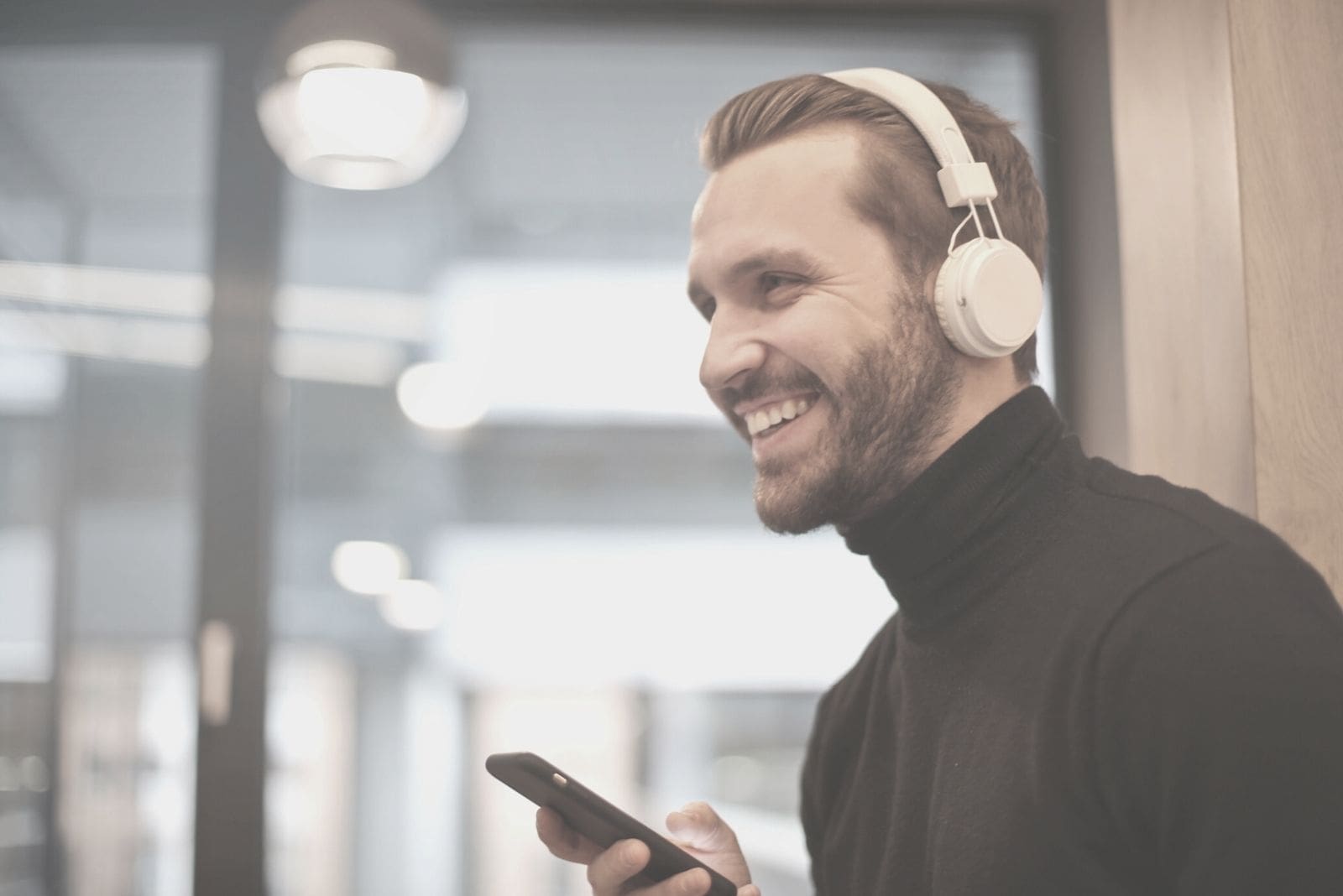man with a headphone smiling and holding a phone indoors