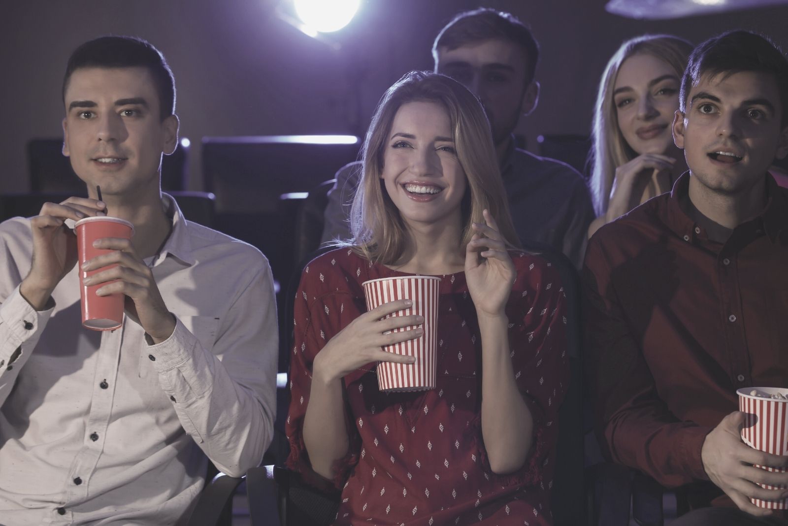 uomini e donne che guardano un film al cinema ridendo e mangiando cibo